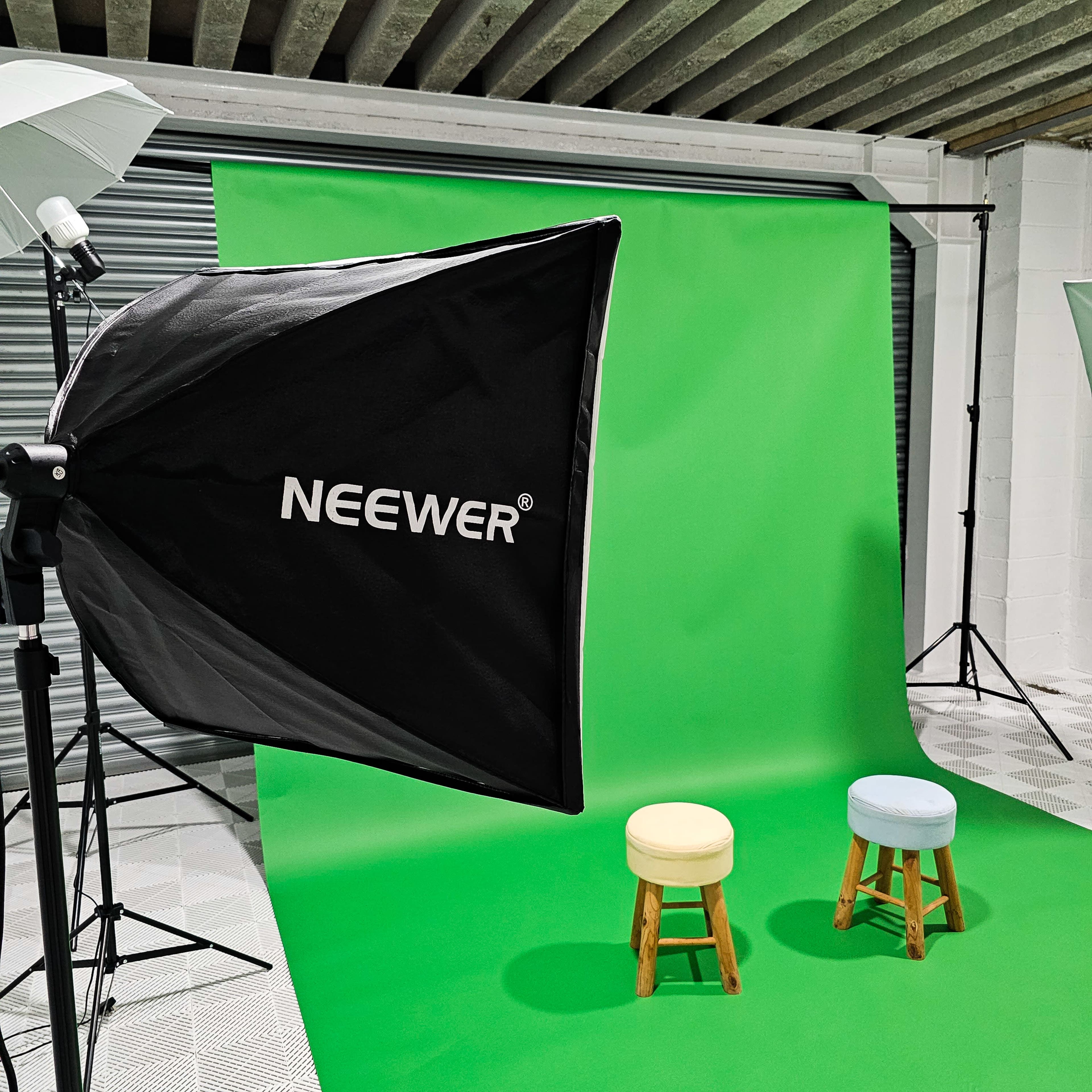 A photography studio with a green backdrop and two wooden stools, one blue and one white, set at the center.