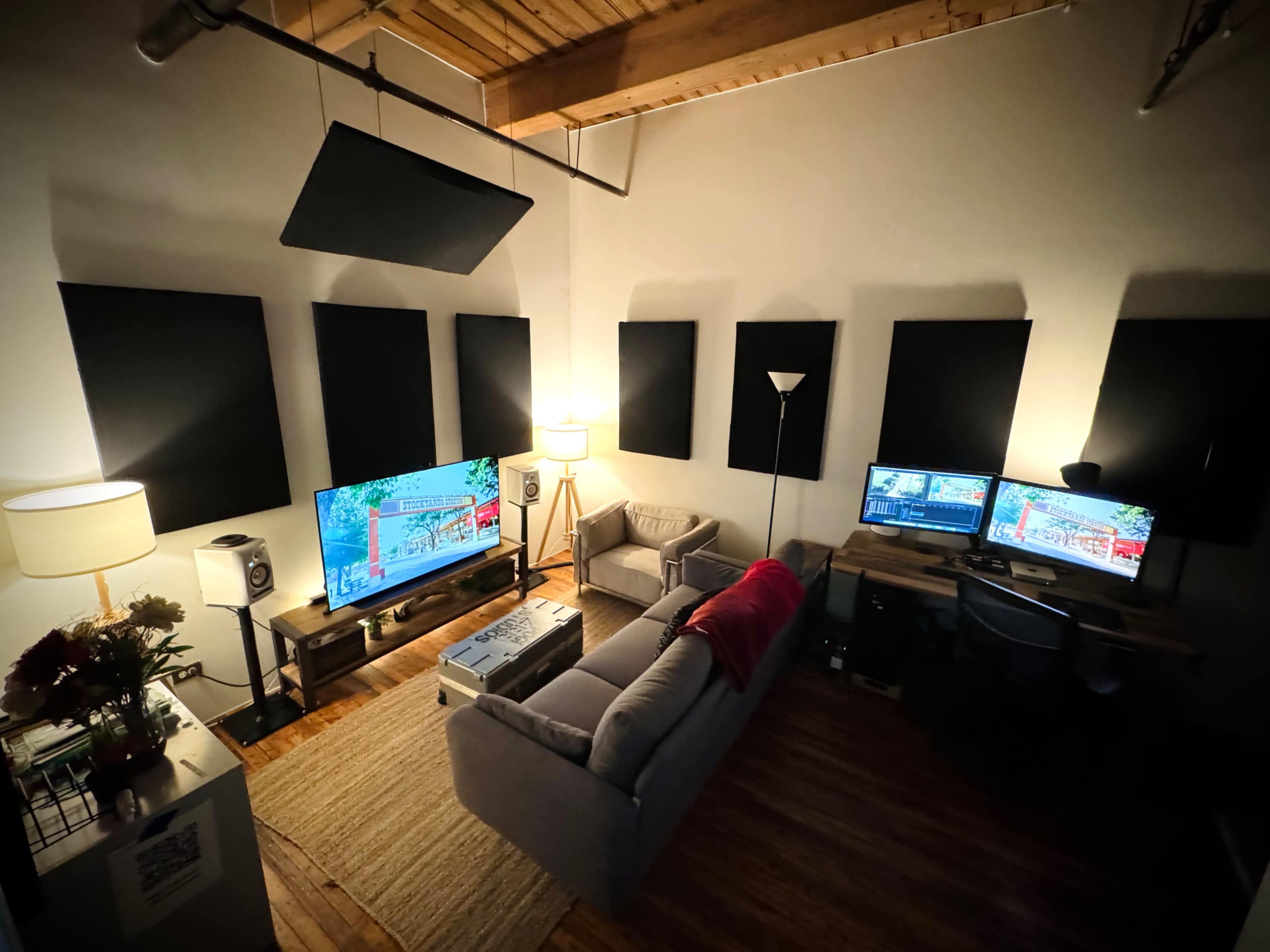 A cozy room features a couch, two televisions, a desk with a computer, and soundproofing panels on the walls.