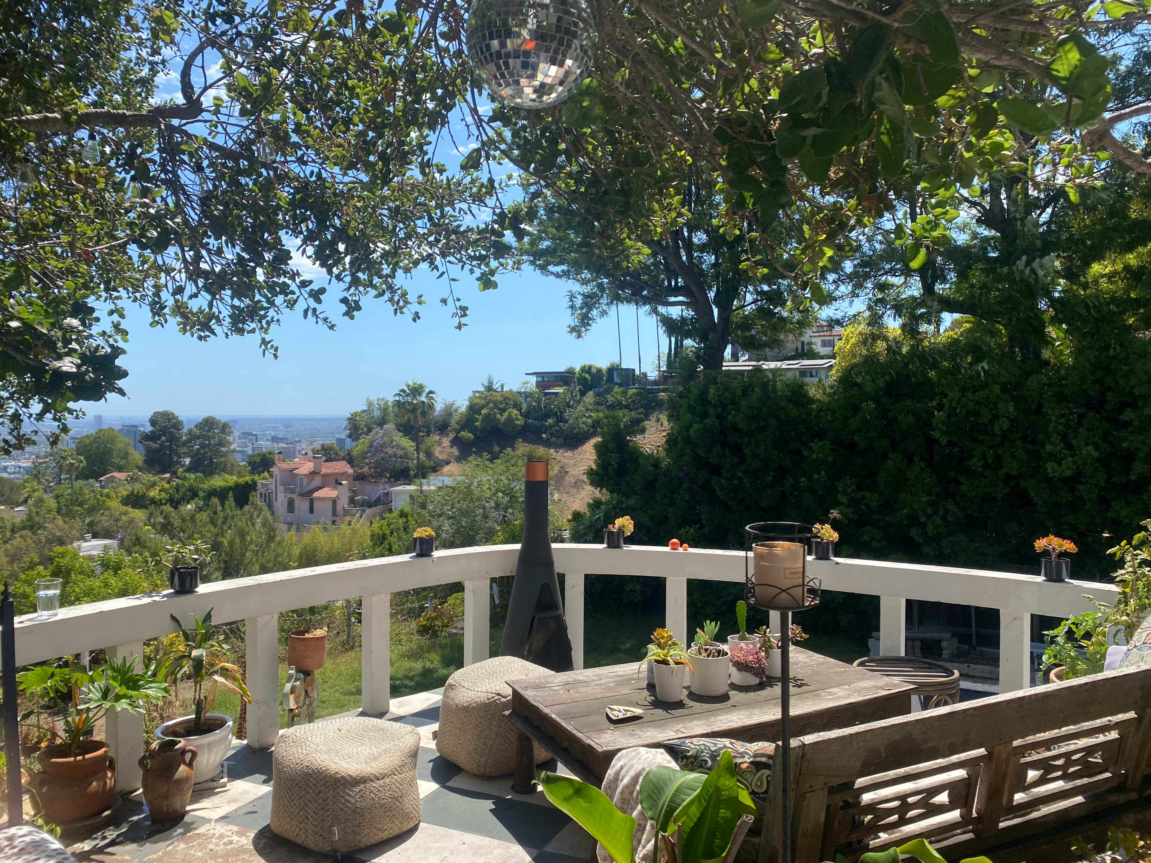 A patio with a table and seating is surrounded by greenery and offers a view of the horizon.