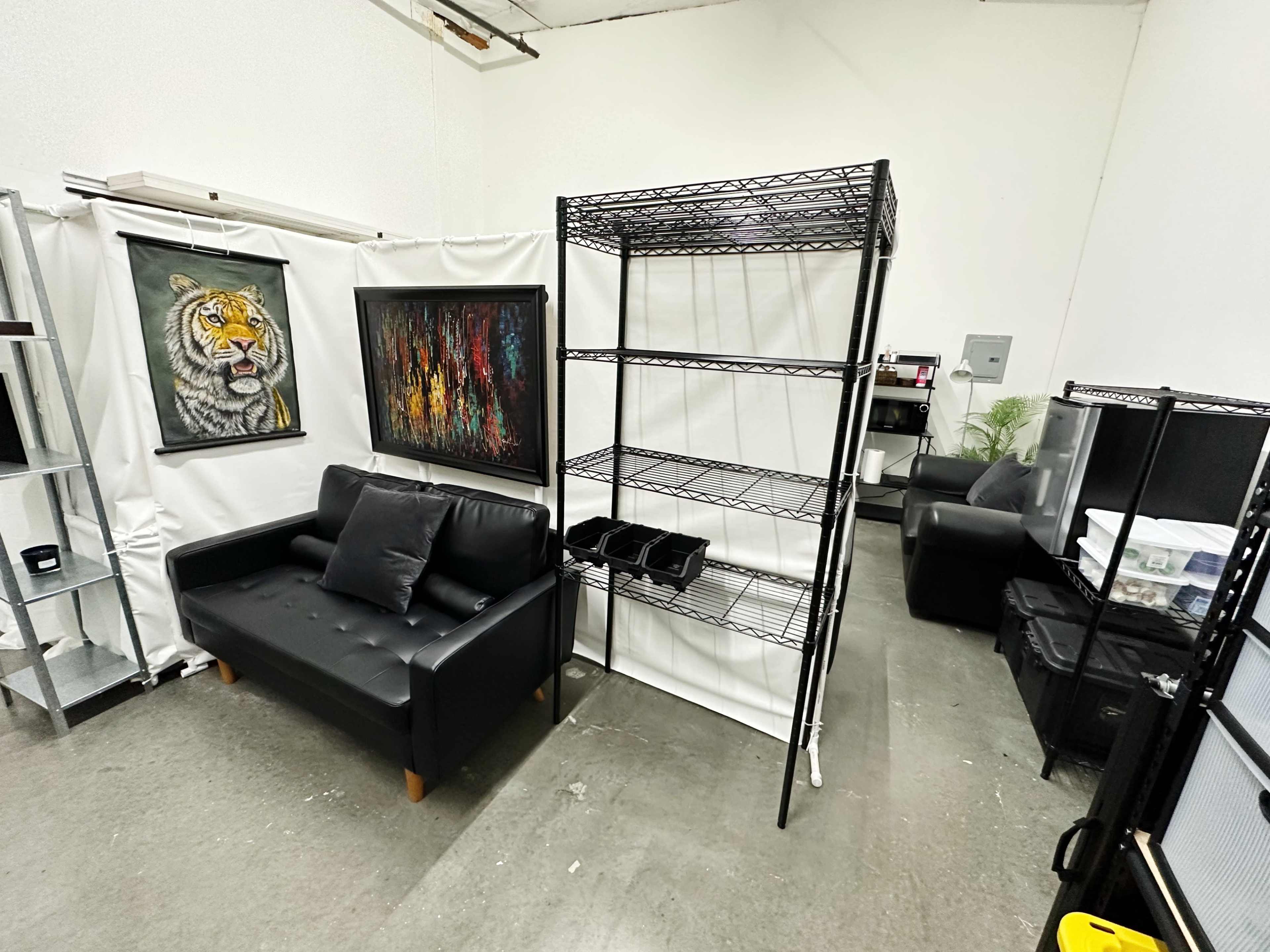 A small room with a black couch, a wire shelving unit, and artwork on the walls.
