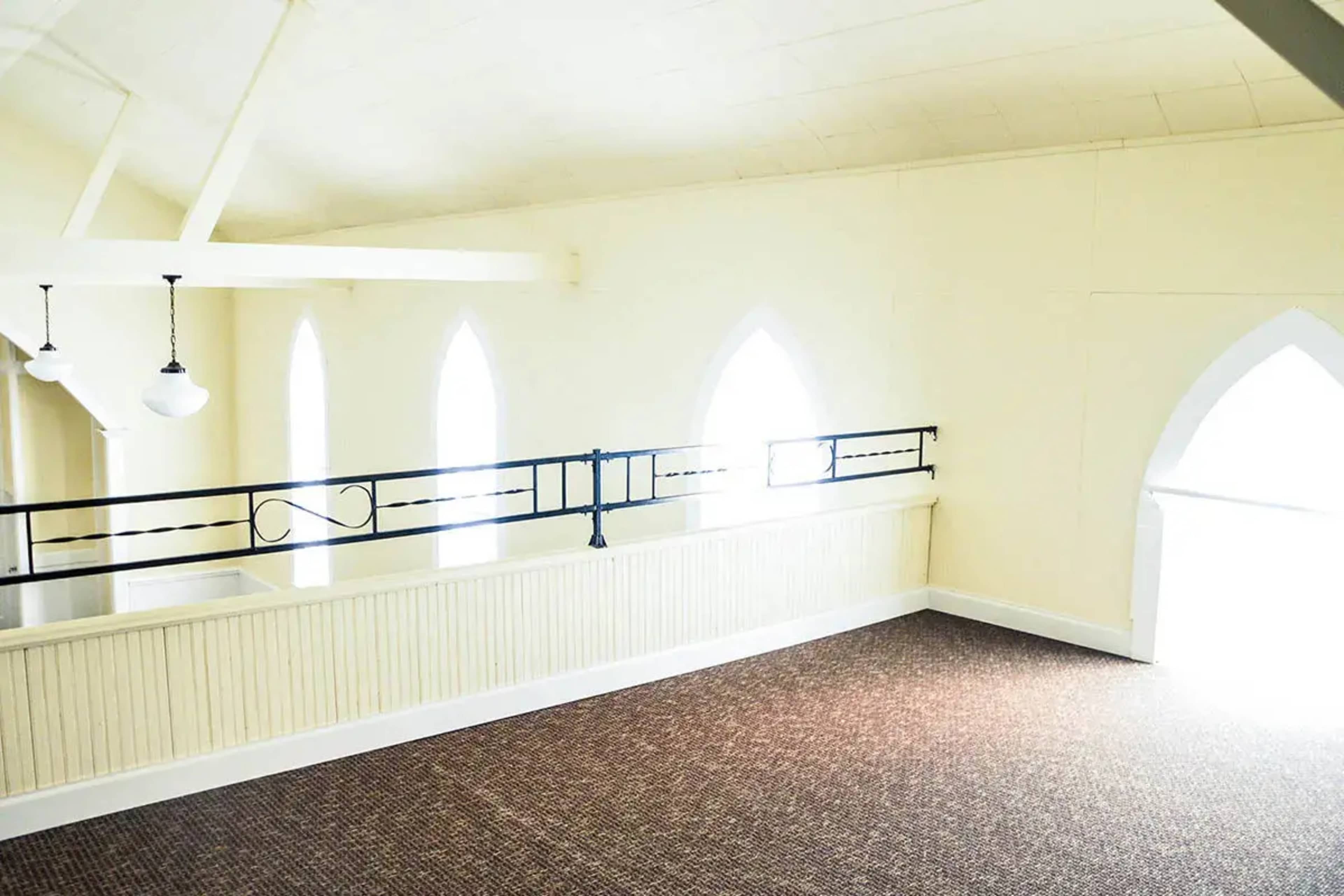 A spacious, empty upper level with a carpeted floor and large arched windows allowing light to enter.