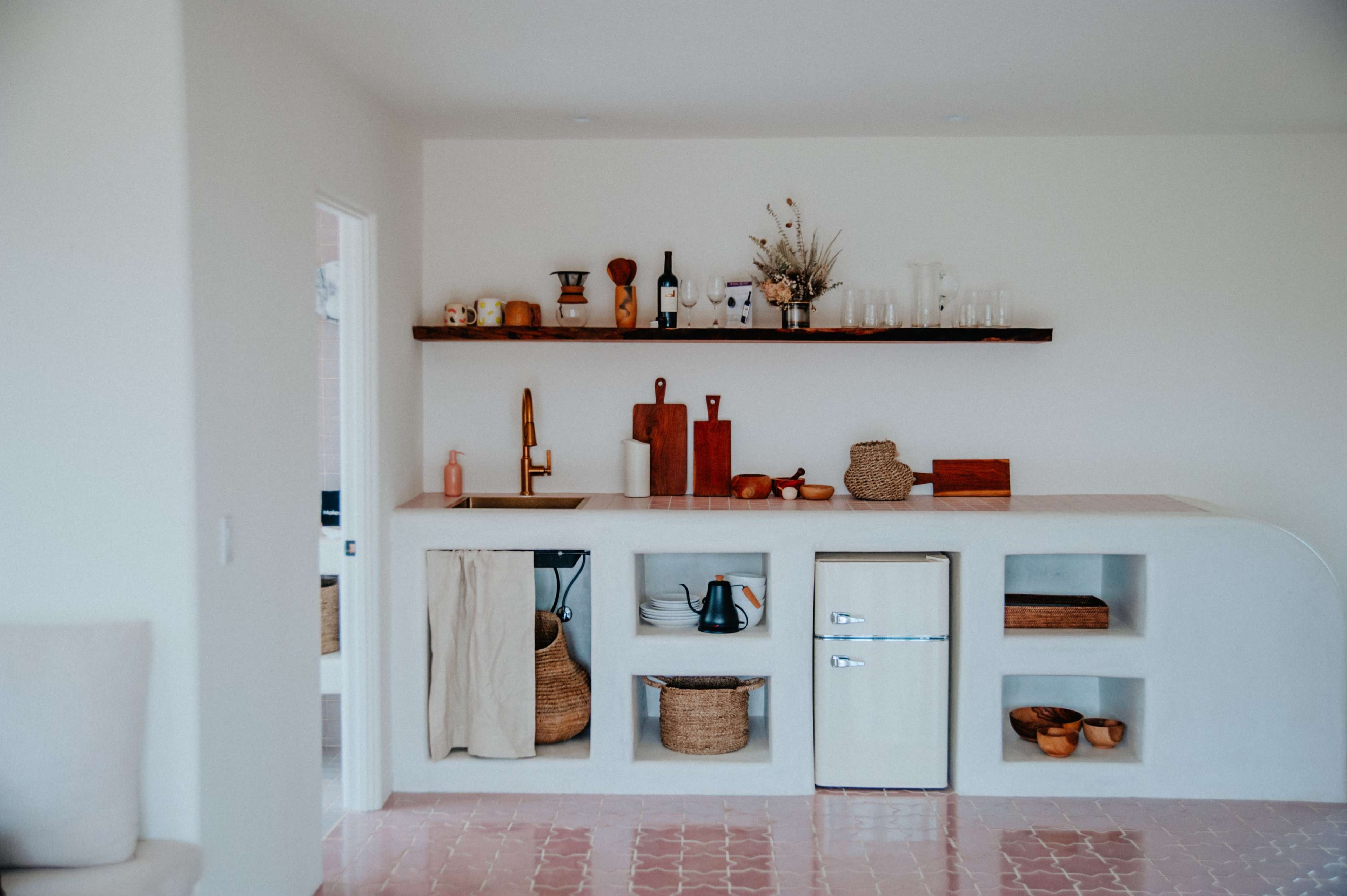 A minimalist kitchen with a curved counter, wooden shelves displaying kitchenware, and various storage baskets.