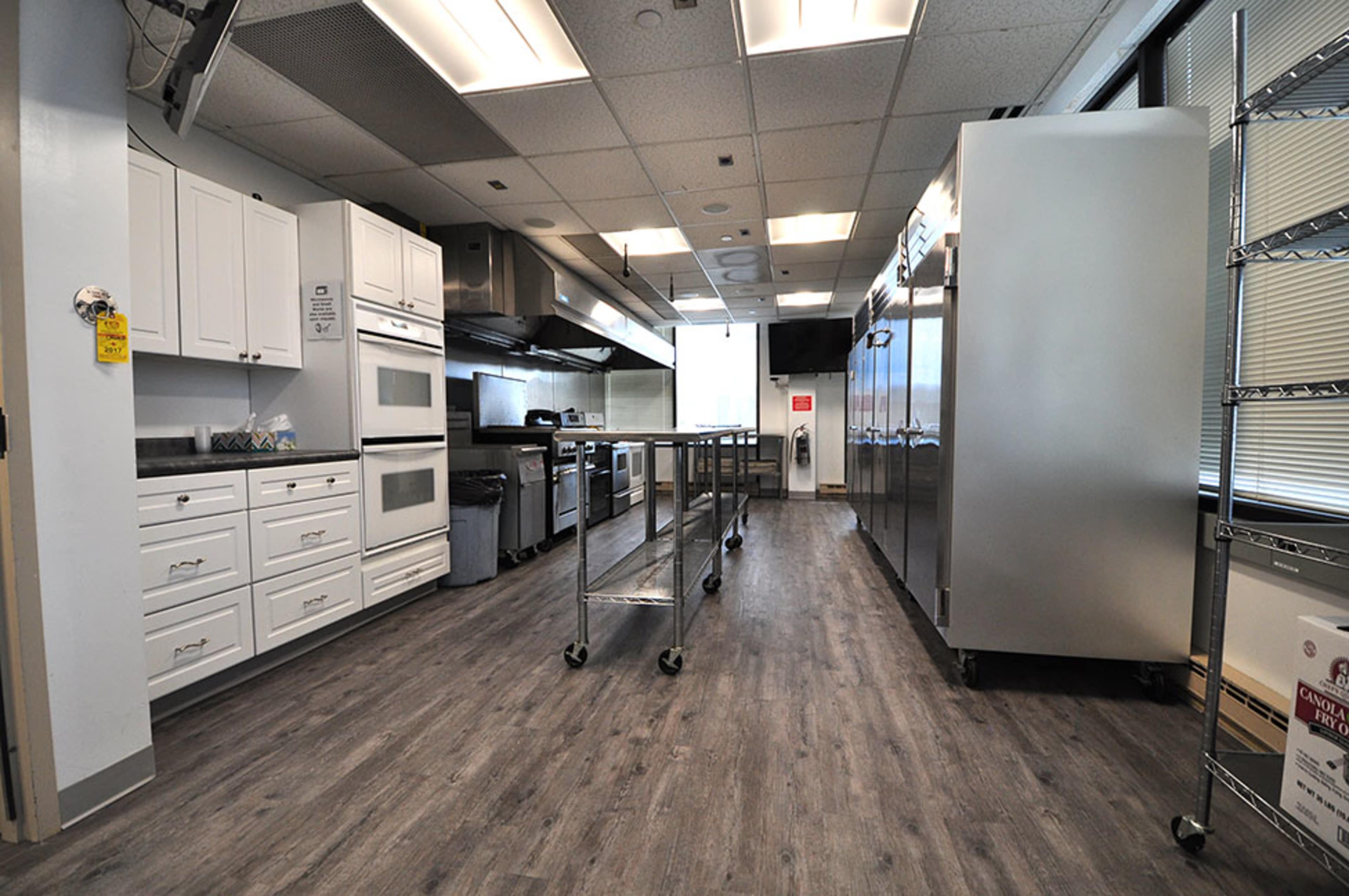 The image shows a modern kitchen with white cabinets, stainless steel appliances, and a series of metal carts positioned along the center of the space.