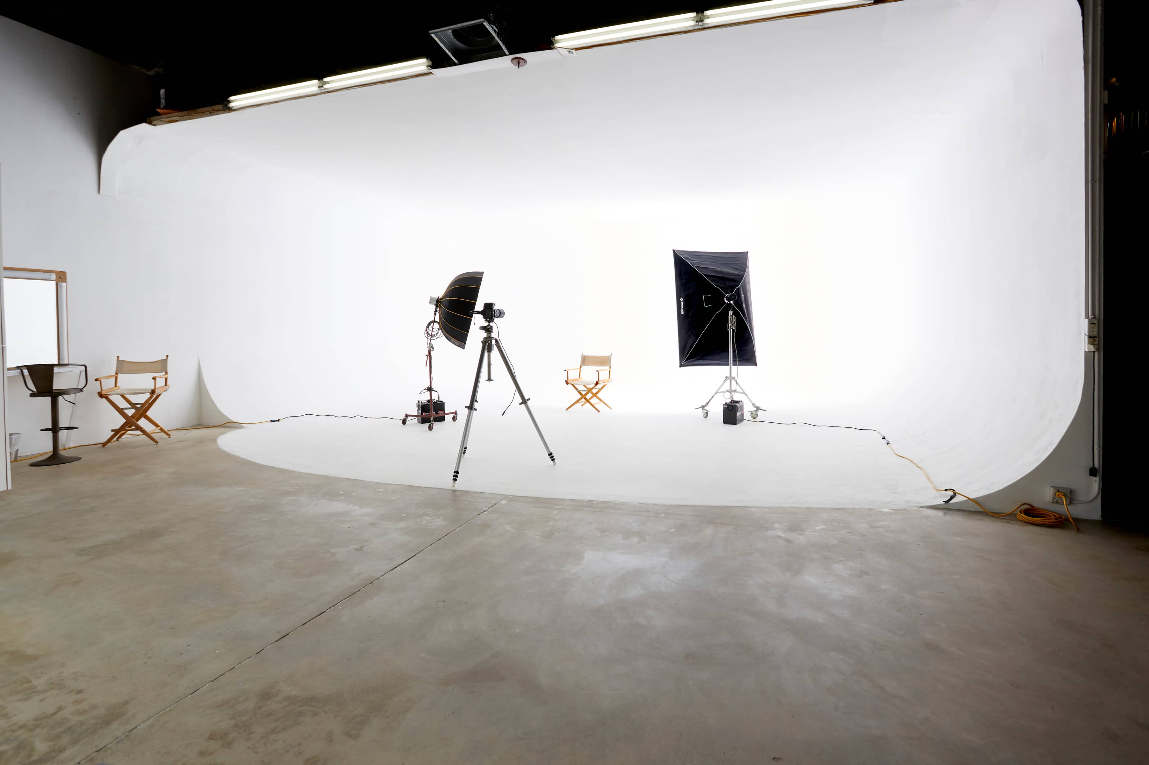 A photography studio features two director's chairs, lighting equipment, and a seamless white backdrop.