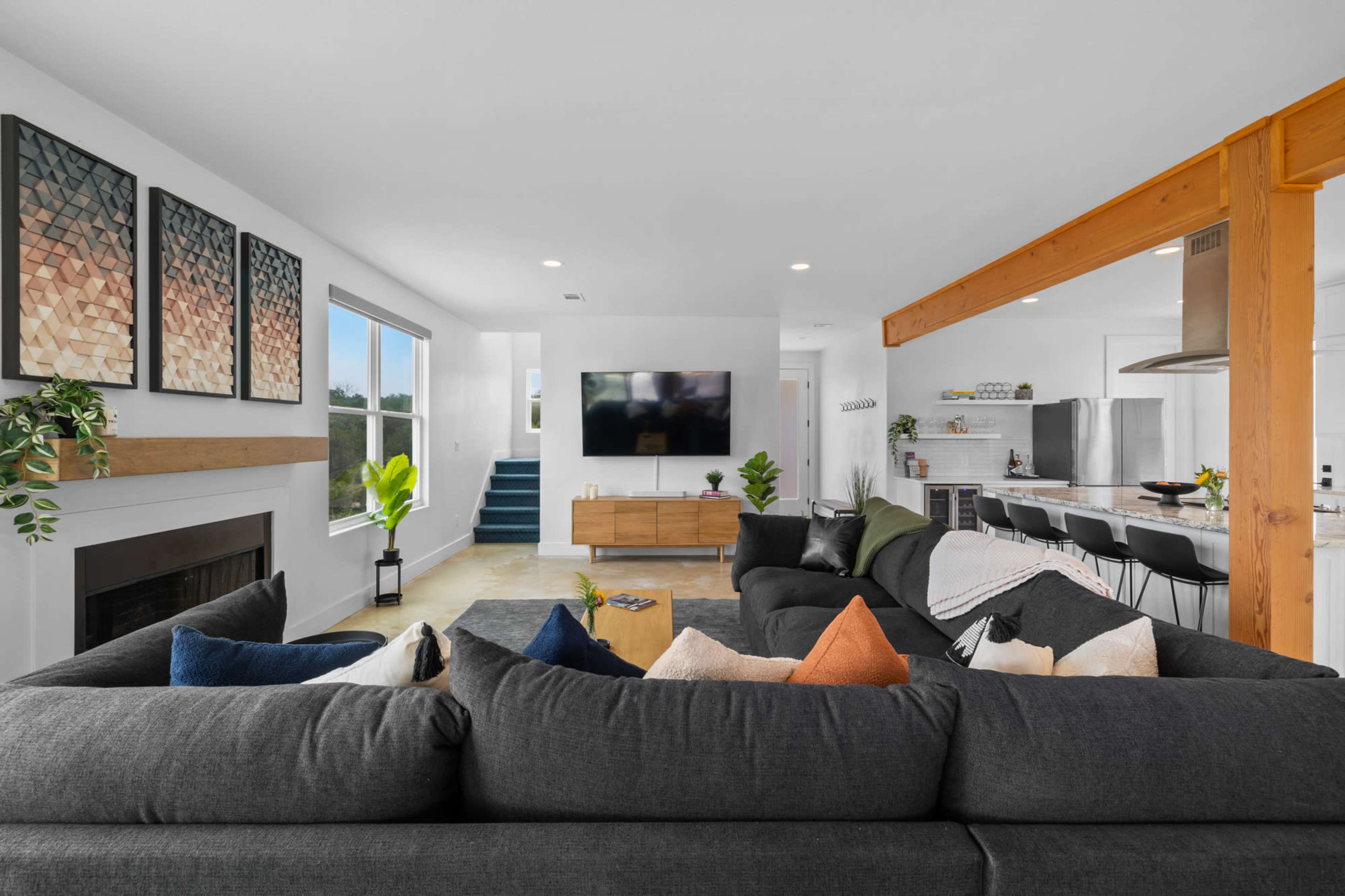A modern living room with a large sectional sofa, a wall-mounted TV, and a kitchen area visible in the background.