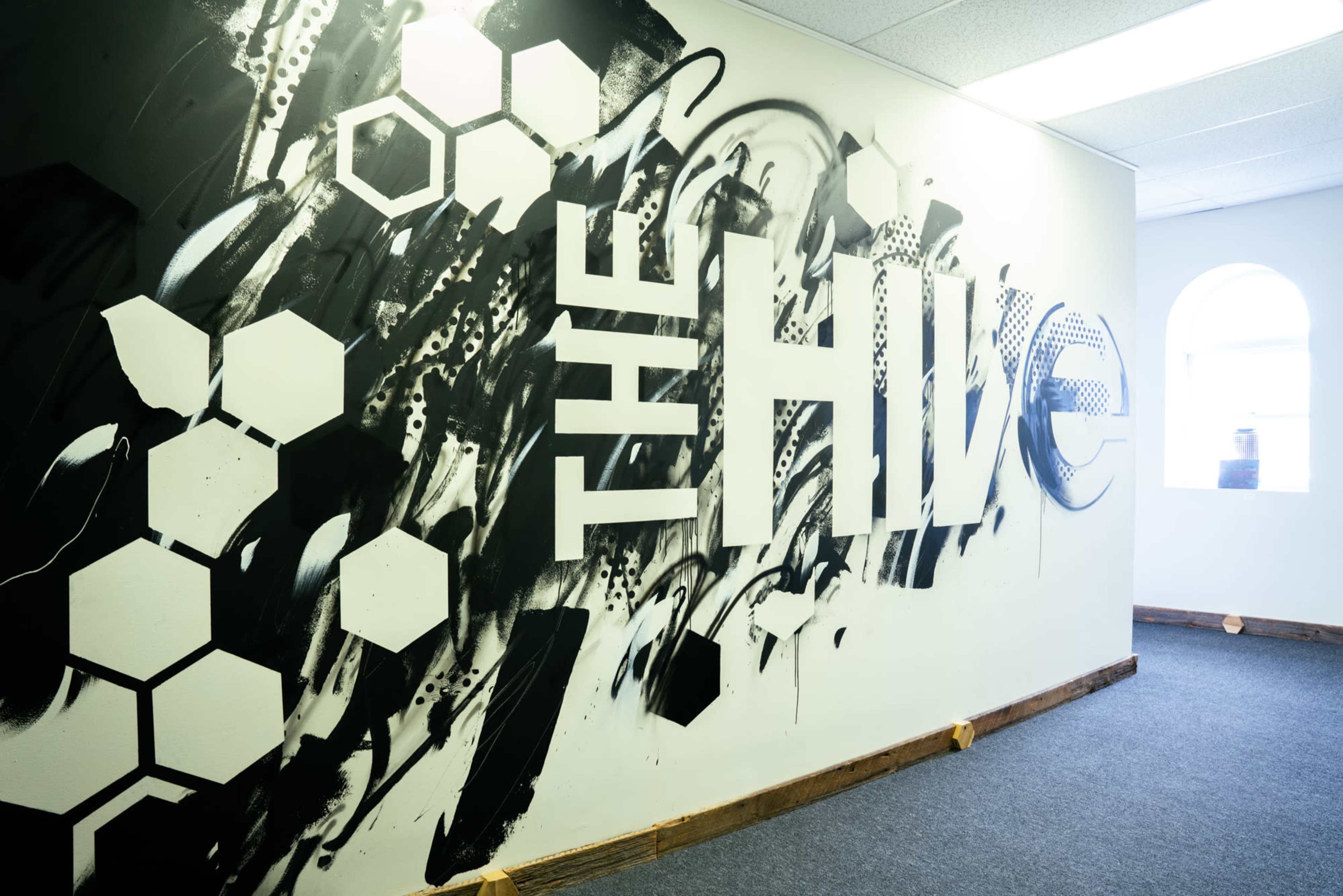 The image shows a wall mural featuring the large text "THE HIVE" alongside abstract black and white designs and hexagonal shapes.