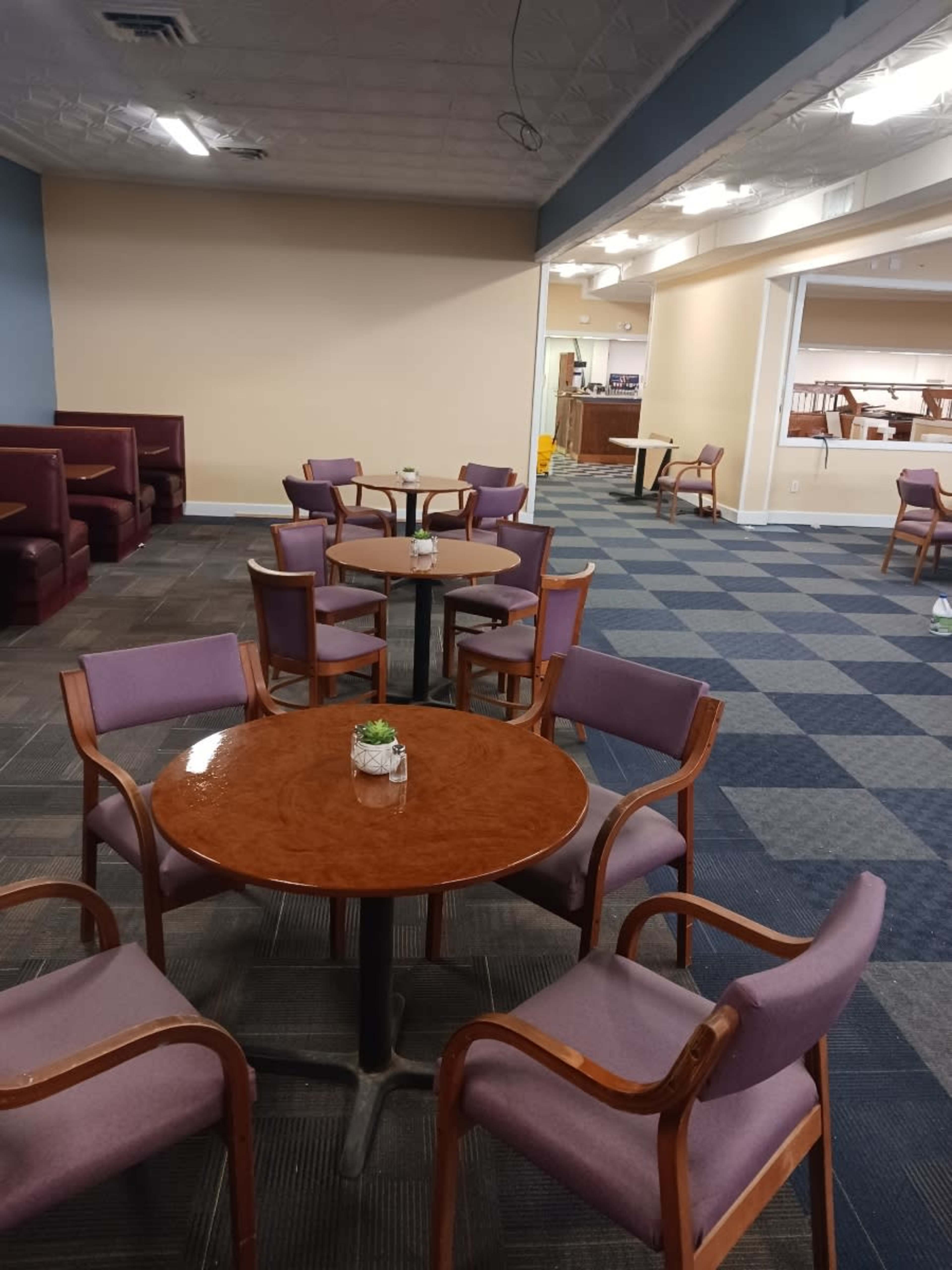 The image shows a spacious, empty seating area with multiple round tables surrounded by chairs, set against a carpeted floor.