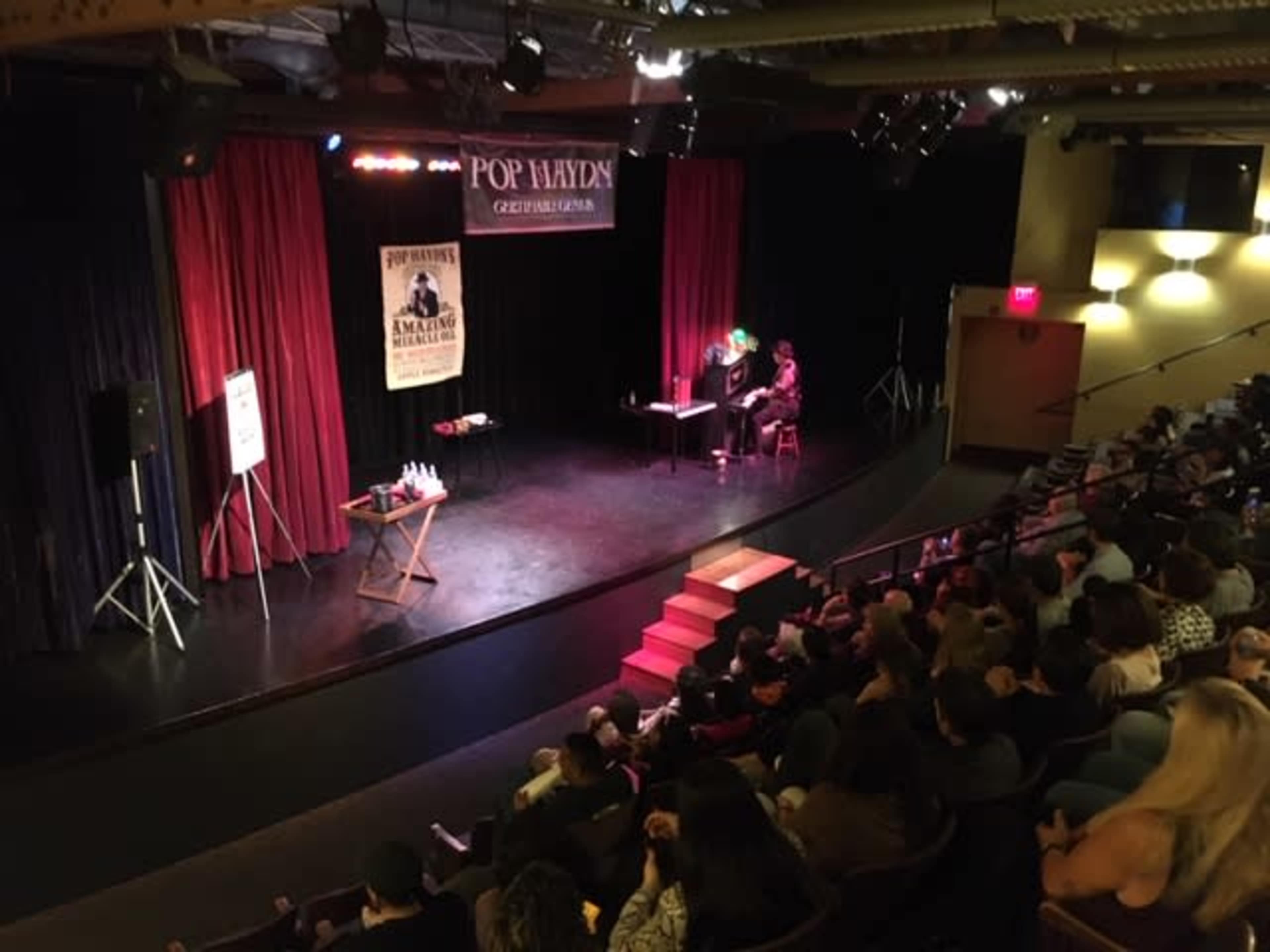 A magician performs on stage in front of an audience seated in a theater.