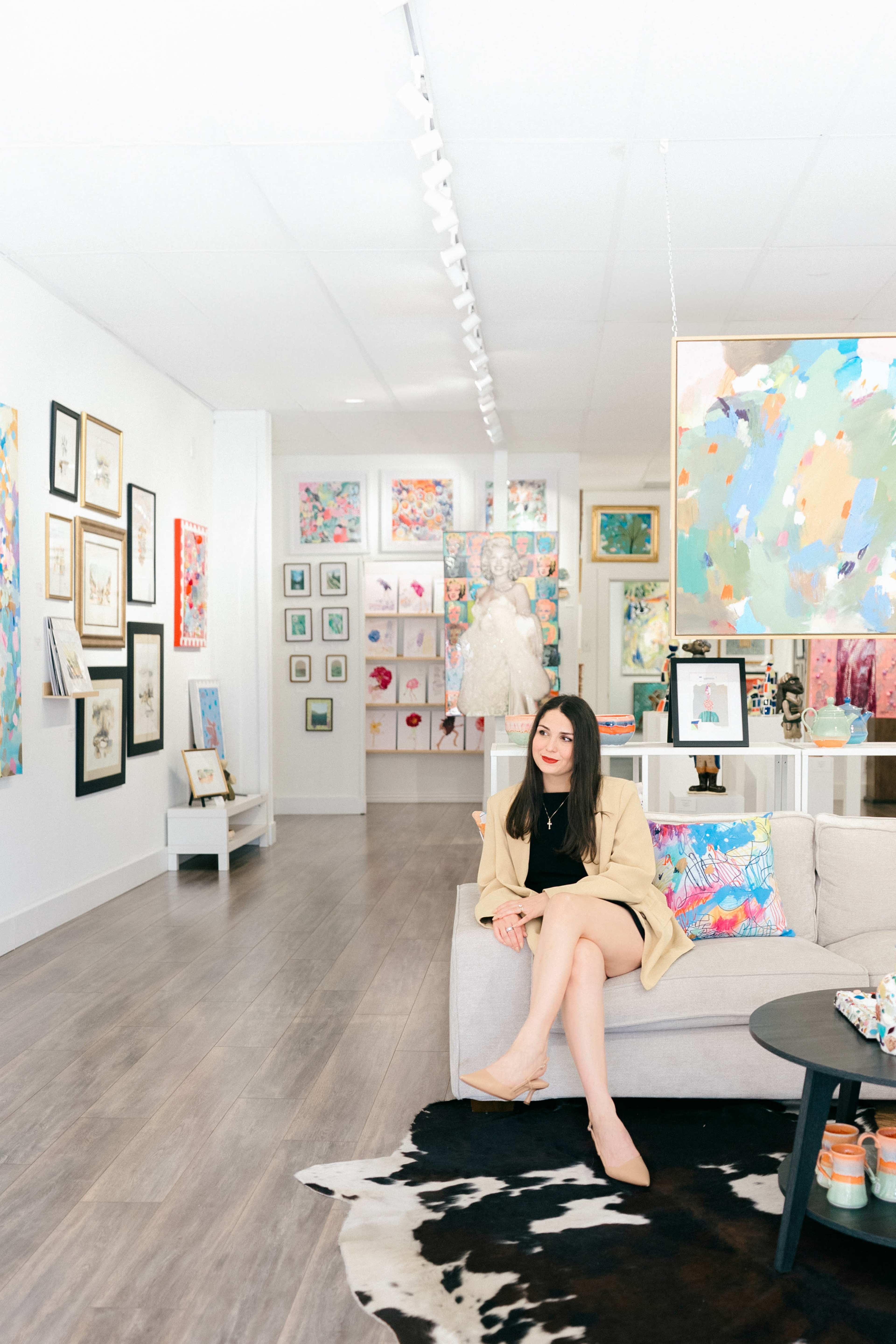A woman sits on a couch in a colorful art gallery surrounded by various artworks on the walls.