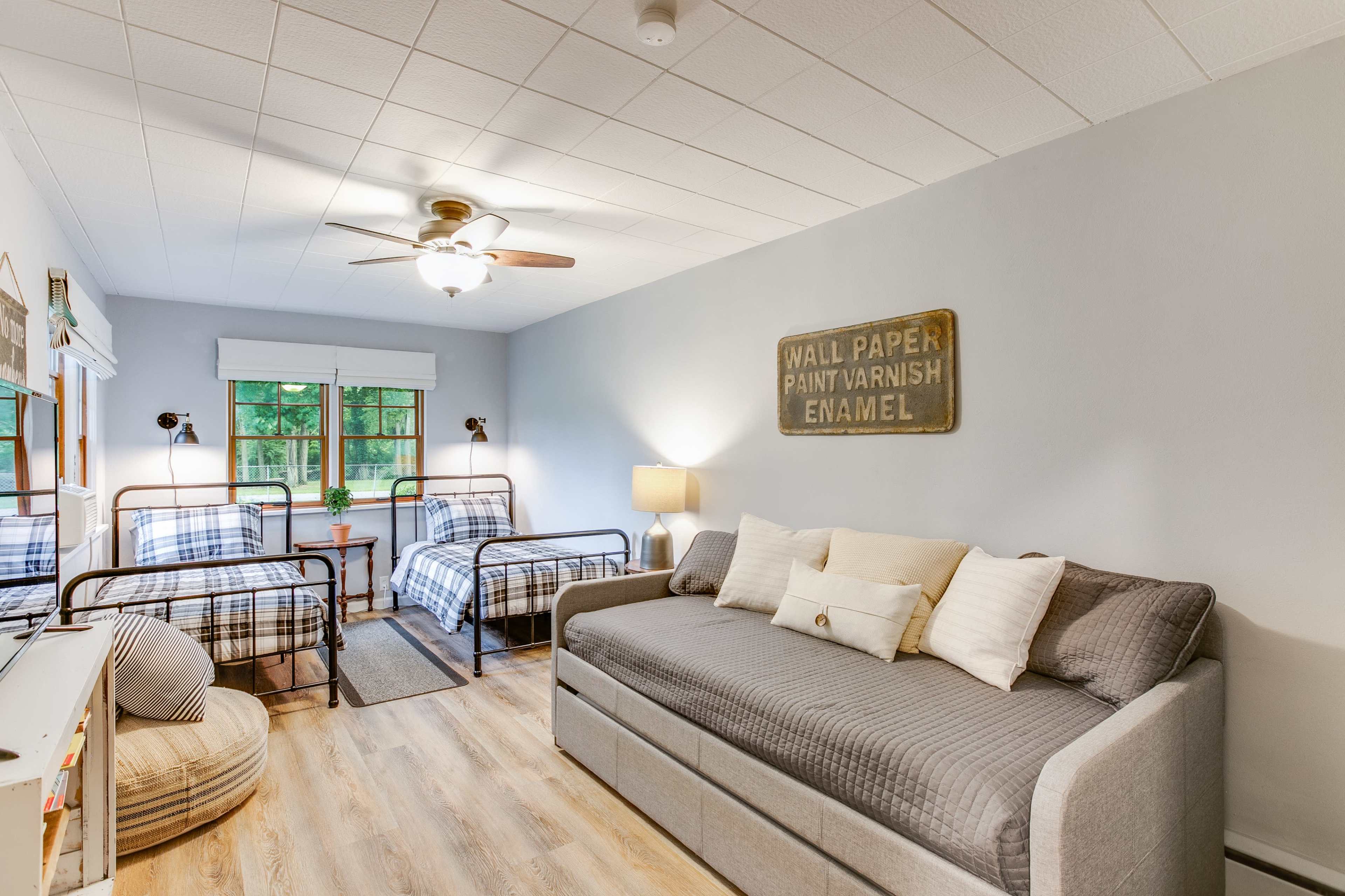 A cozy bedroom with two metal frame beds, a daybed, a lamp, and a wall sign, all set against a light blue wall.