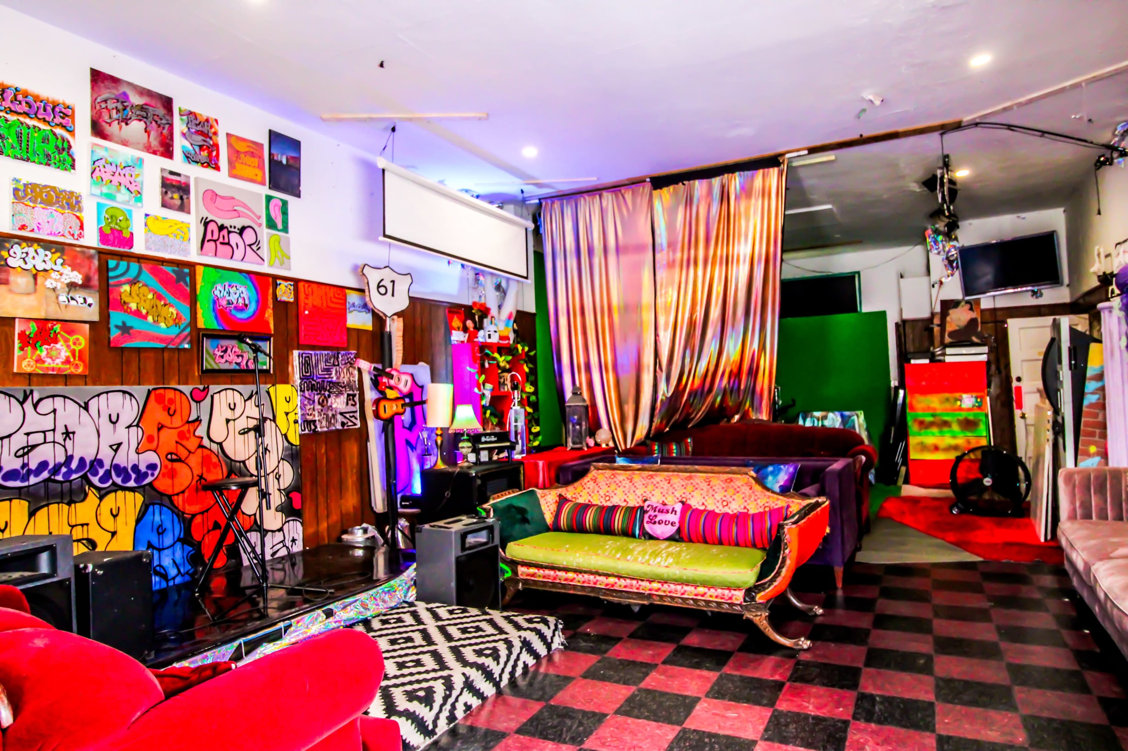 A vibrant, eclectic lounge area featuring colorful art on the walls, various seating options, and a stage-like setup at one end.