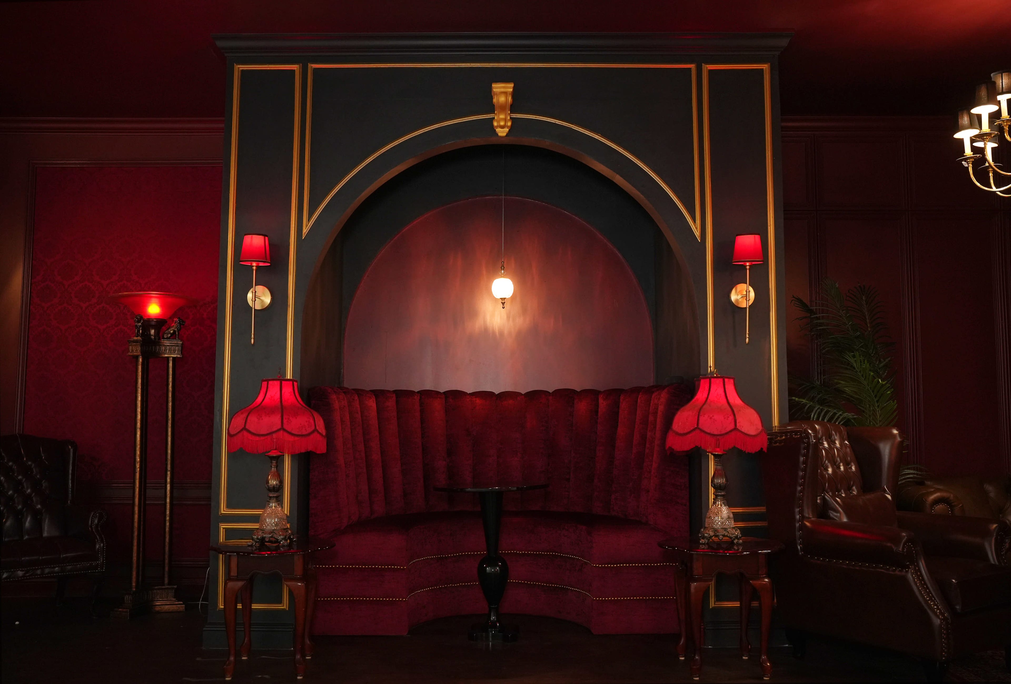 A velvet upholstered seating area with red lamps and a circular wall feature in a richly decorated room.