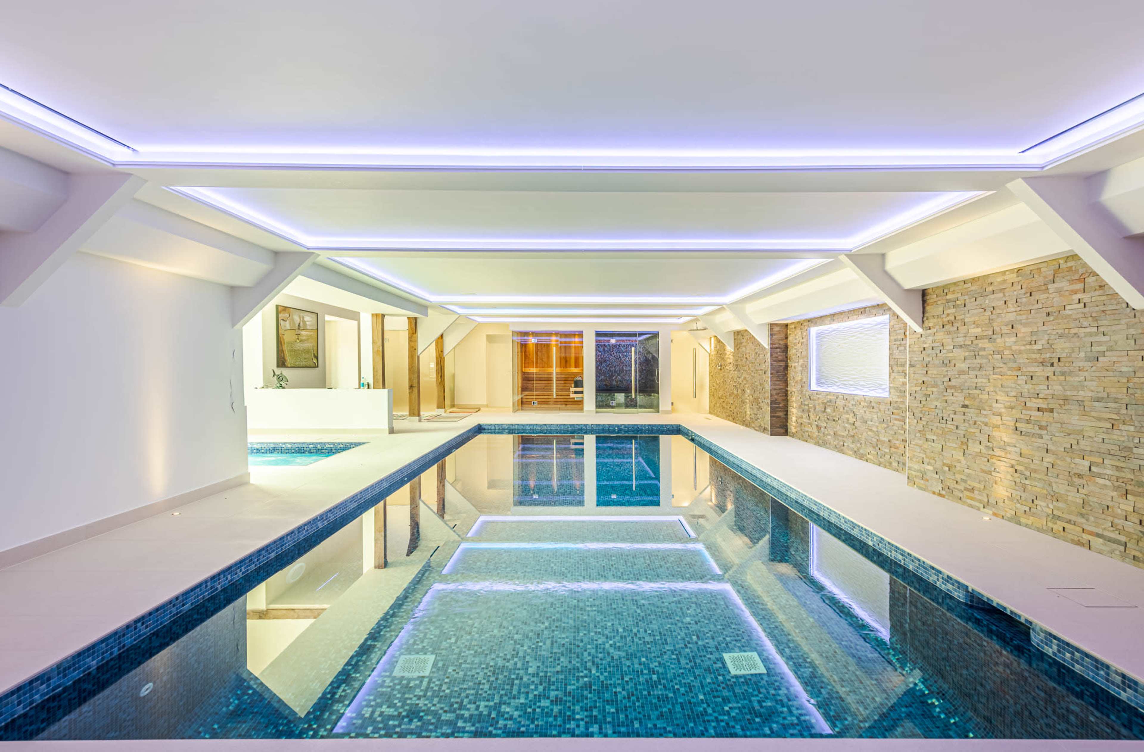 The image shows a modern indoor swimming pool enclosed by stone walls and illuminated by recessed lighting.