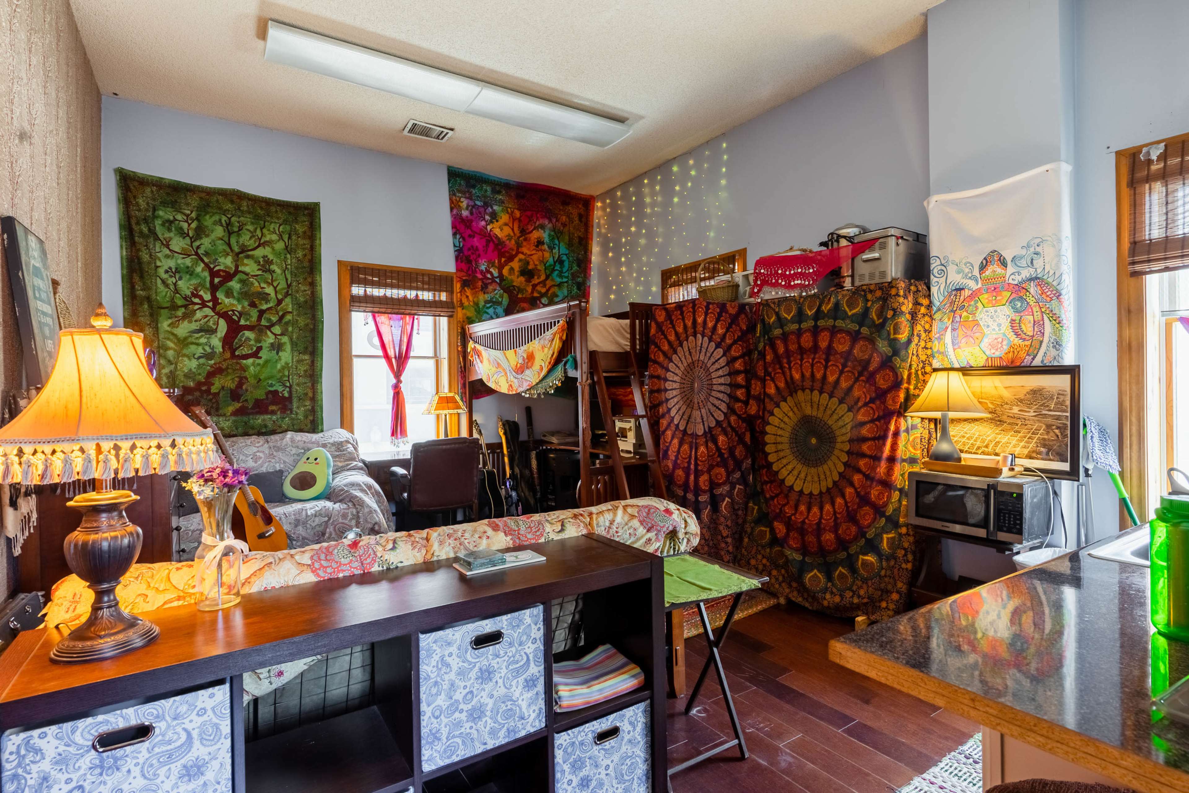 The image depicts a cozy room filled with colorful tapestries, a guitar, and various furniture pieces arranged around a central space.
