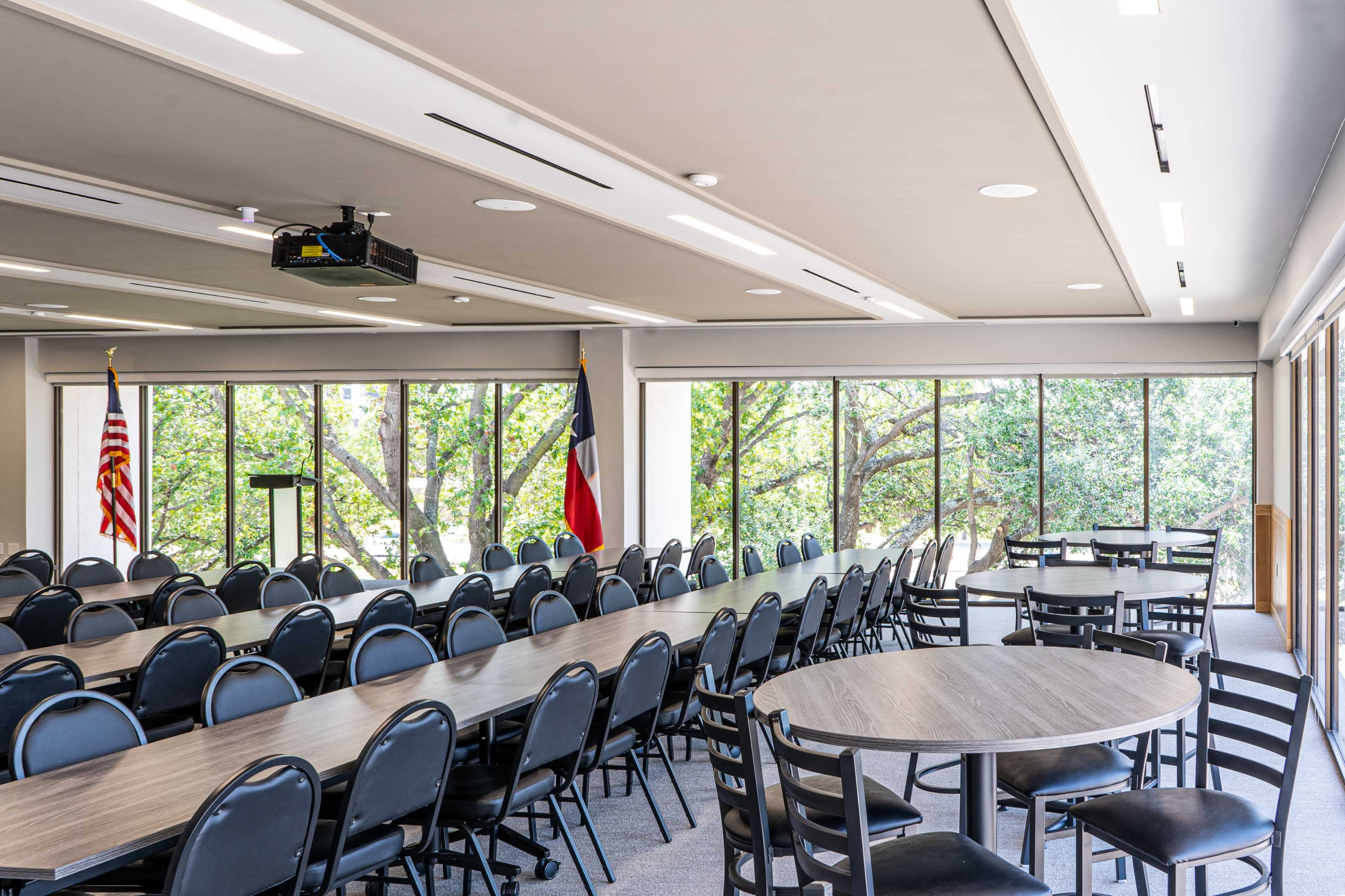 A conference room features multiple tables and chairs arranged in a way that accommodates attendees, with large windows providing a view of the outdoors.