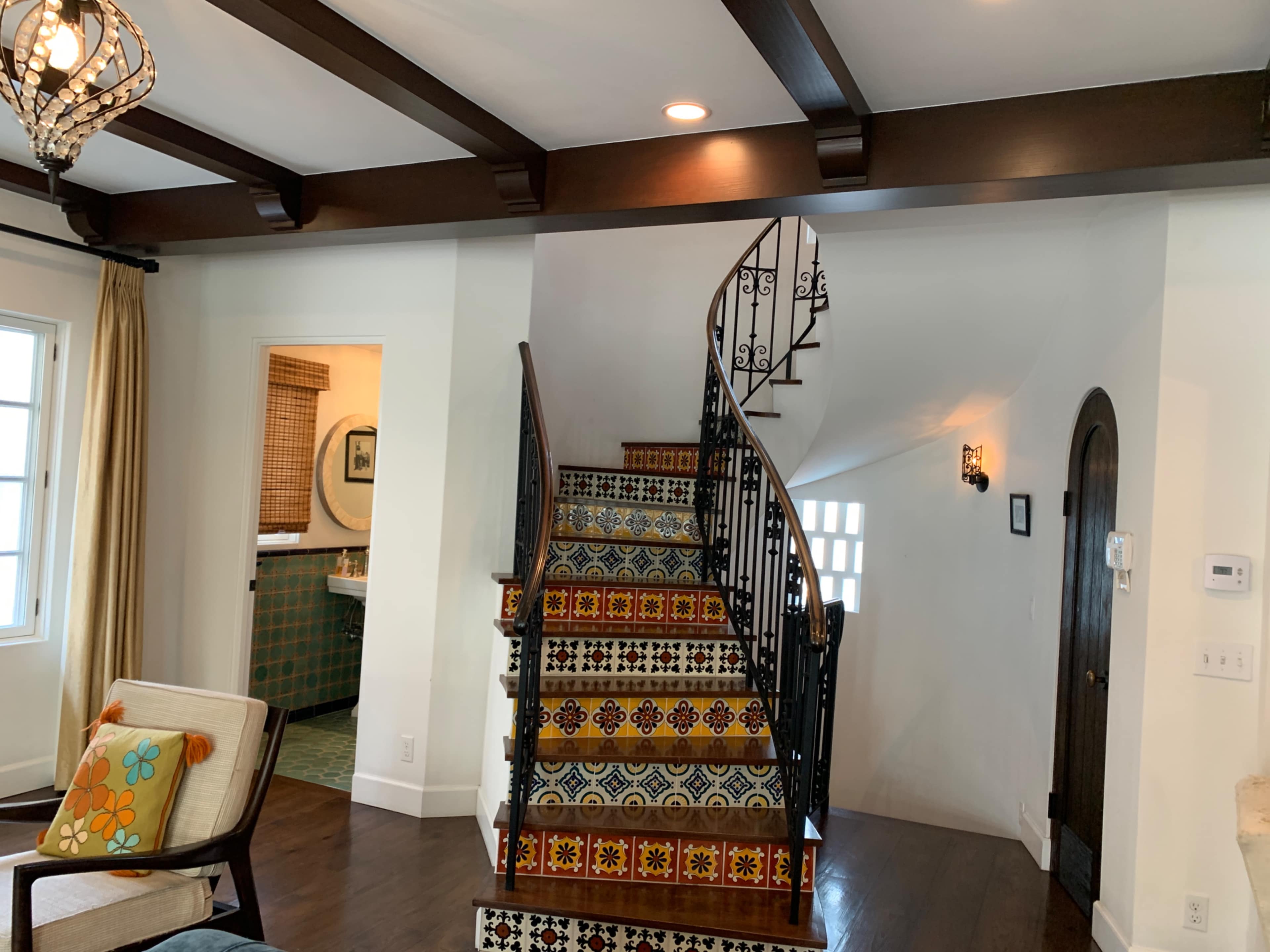 A staircase with decorative tile leading up, surrounded by a white wall and dark wooden beams overhead.