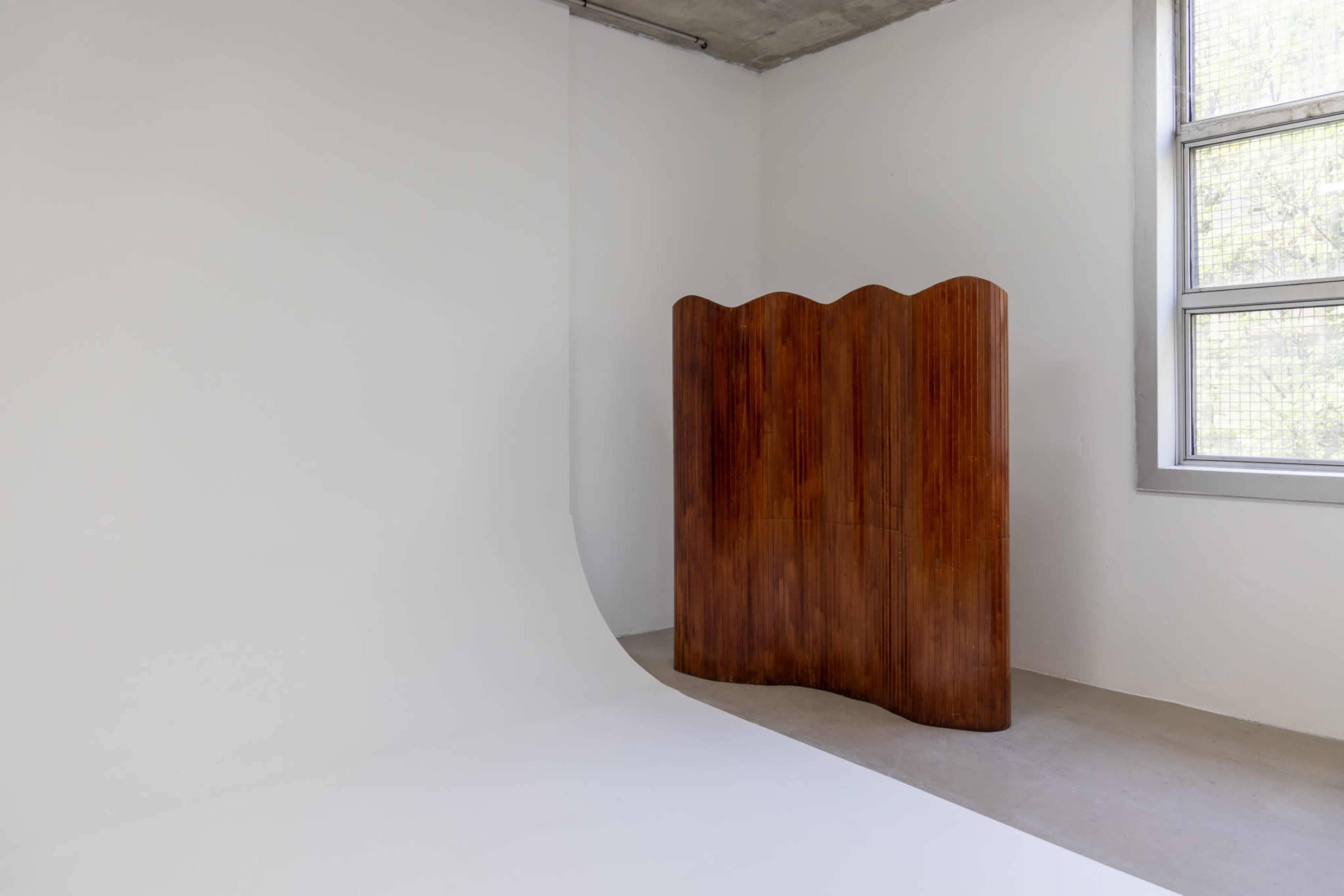 The image shows a wooden room divider with a wavy top set against a plain white wall in a well-lit space.