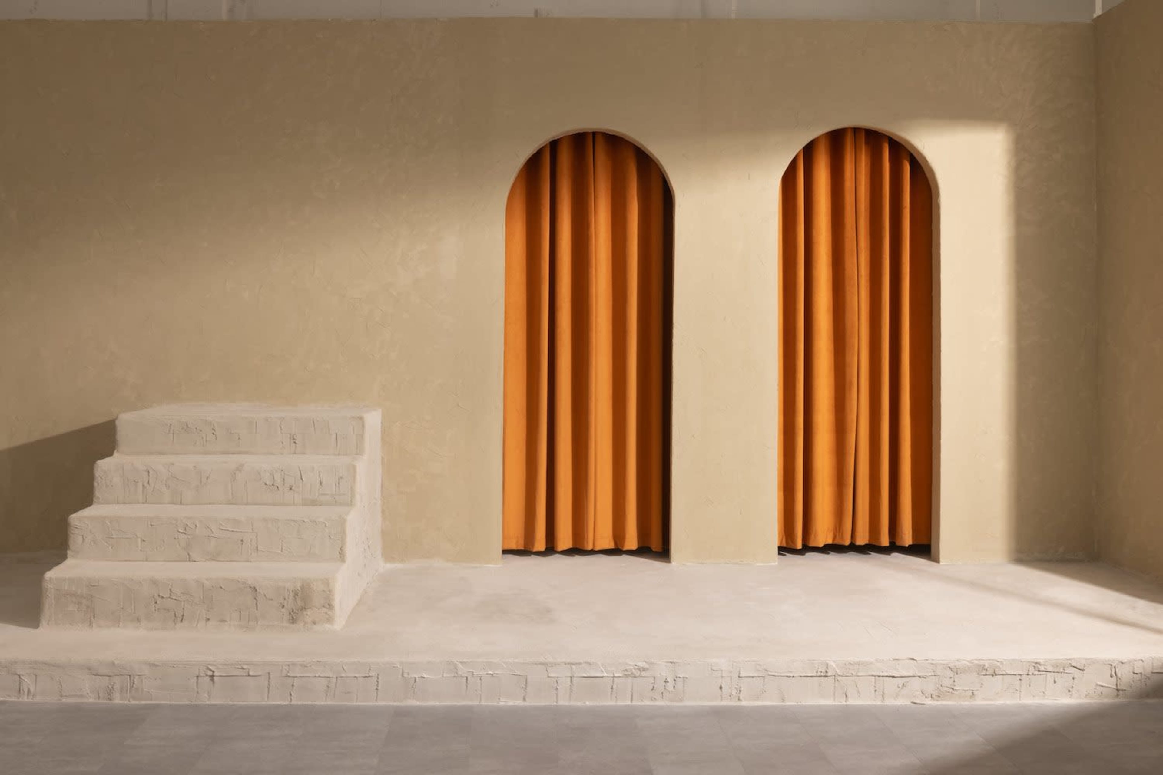 A minimalist interior featuring two arched openings with orange curtains, flanked by a set of stairs against a textured, neutral wall.