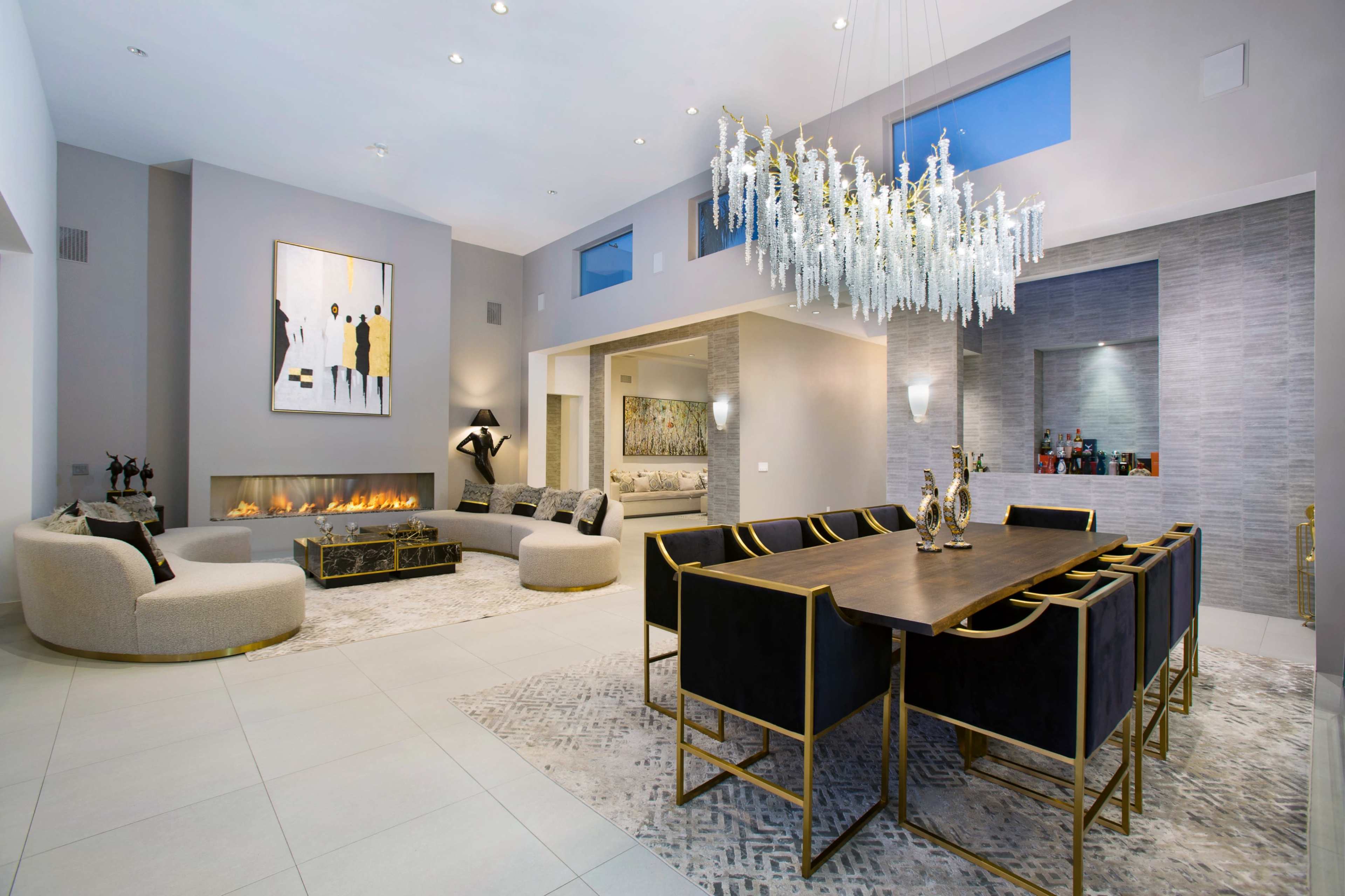 The image shows a modern open-concept living and dining area with a chandelier, decorative artwork, and a fireplace.