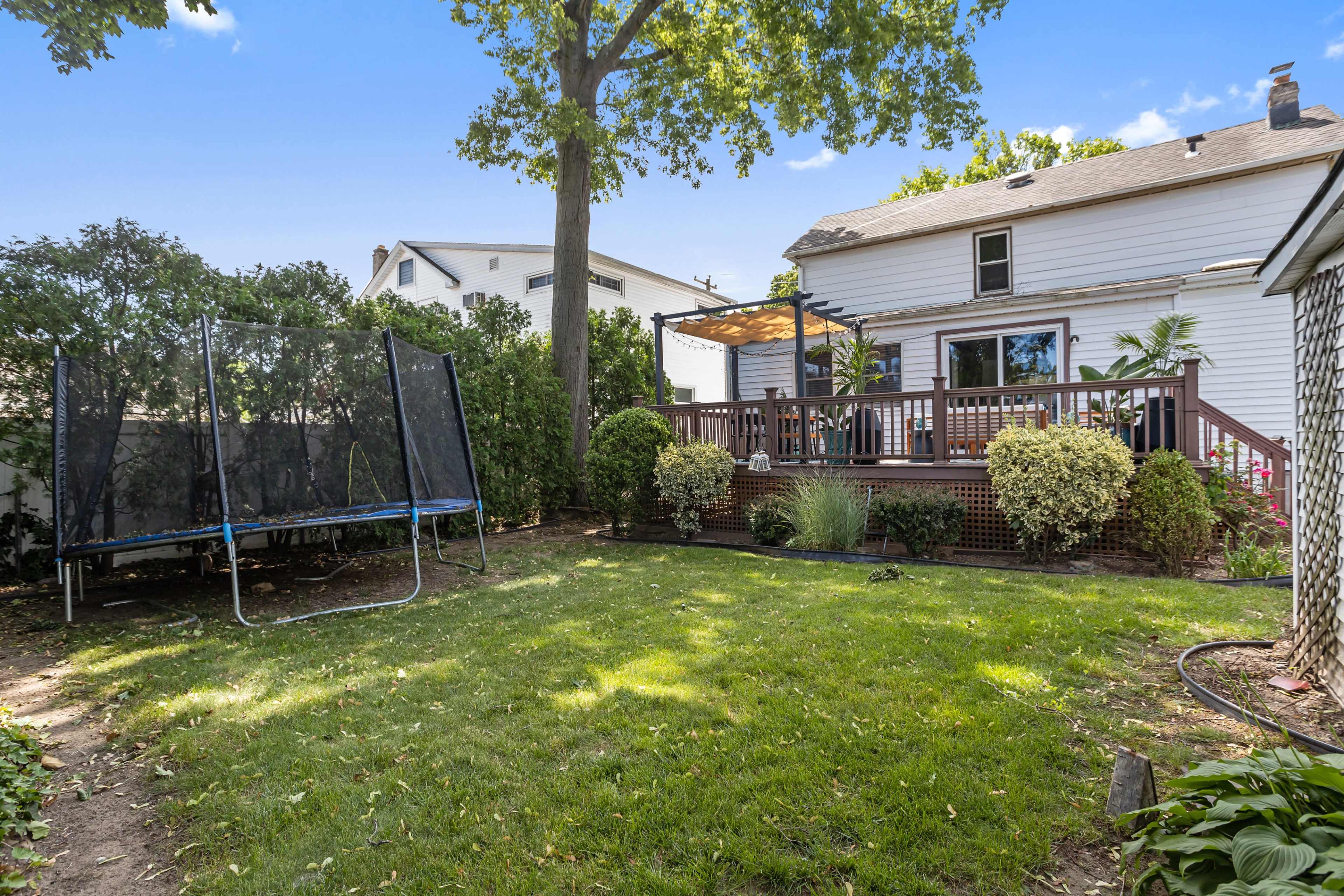 The image shows a backyard with a wooden deck, a trampoline, and well-maintained grass and shrubs.