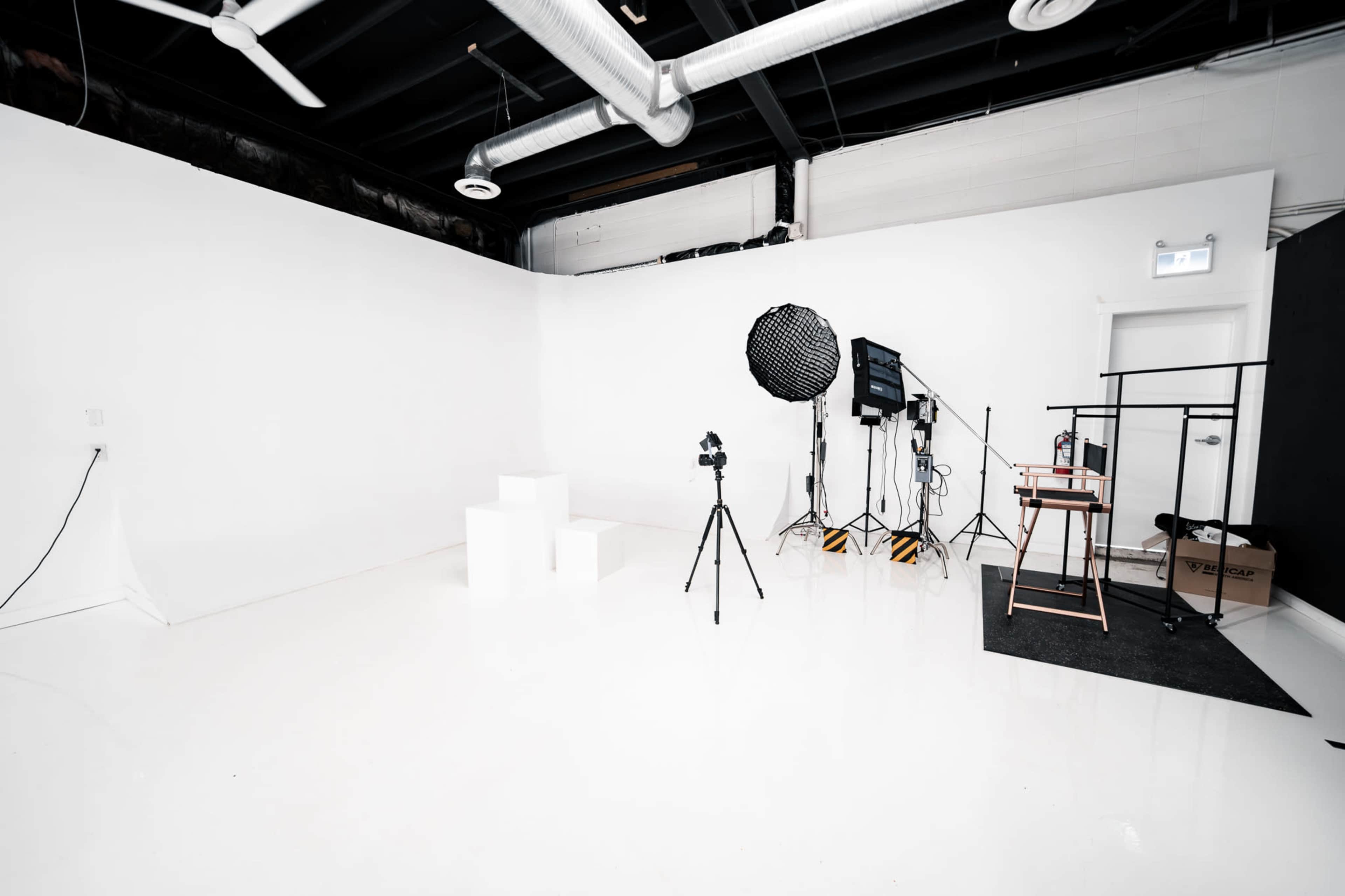 The image shows a photography studio featuring white walls, a glossy floor, and equipment including tripods, lights, and a backdrop.