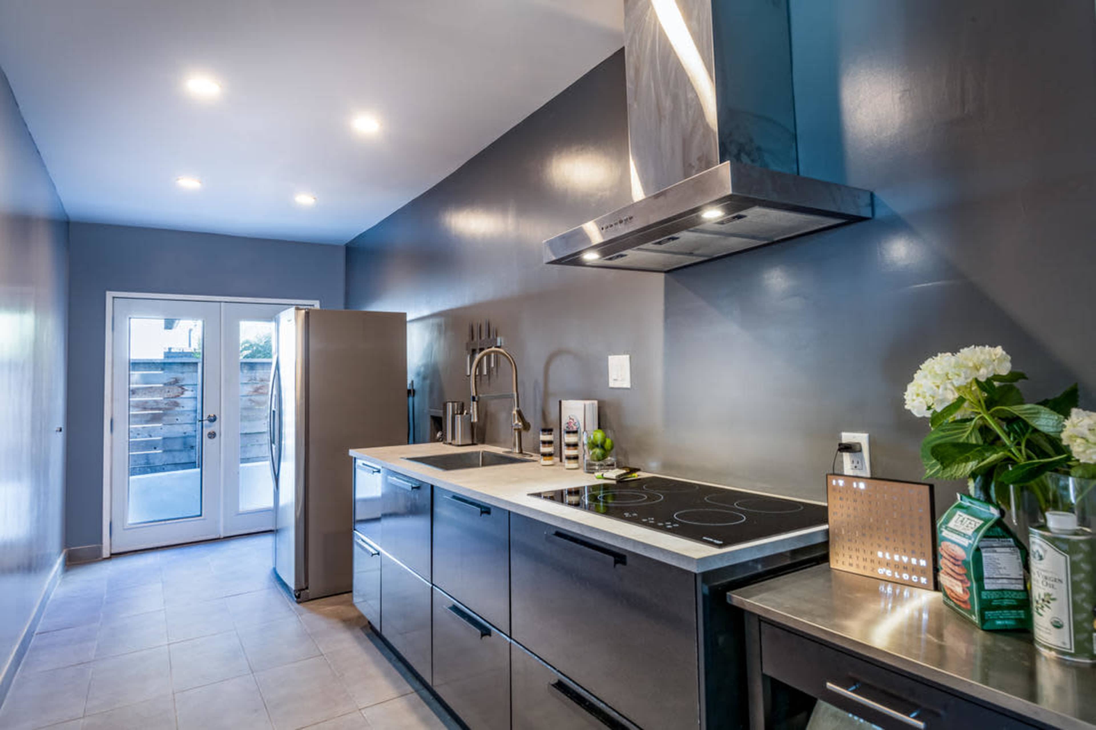 A modern kitchen features stainless steel appliances, a sleek countertop with an induction cooktop, and a door leading to an outdoor space.