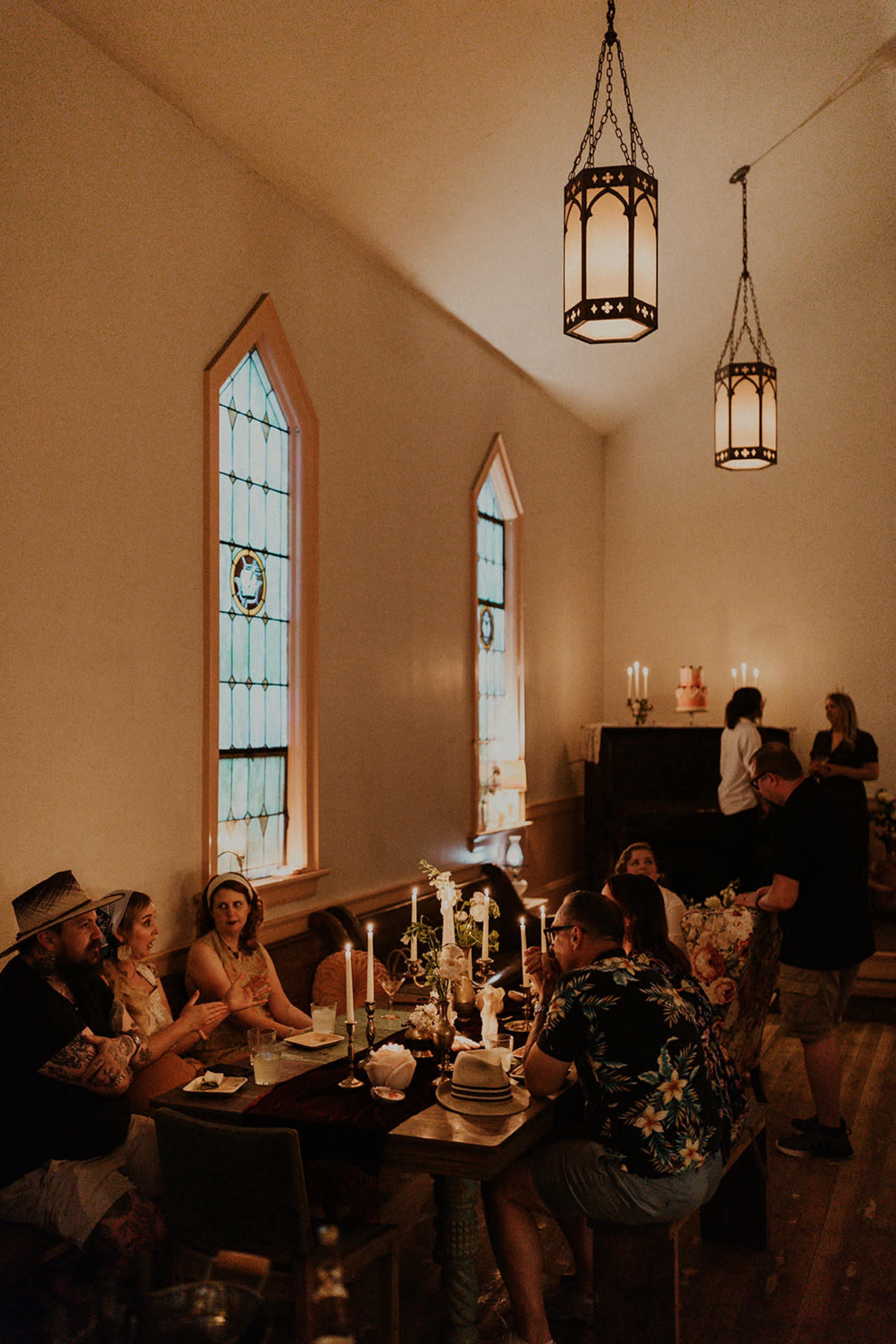A group of people sits around a table in a dimly lit room with stained glass windows and candlelight.