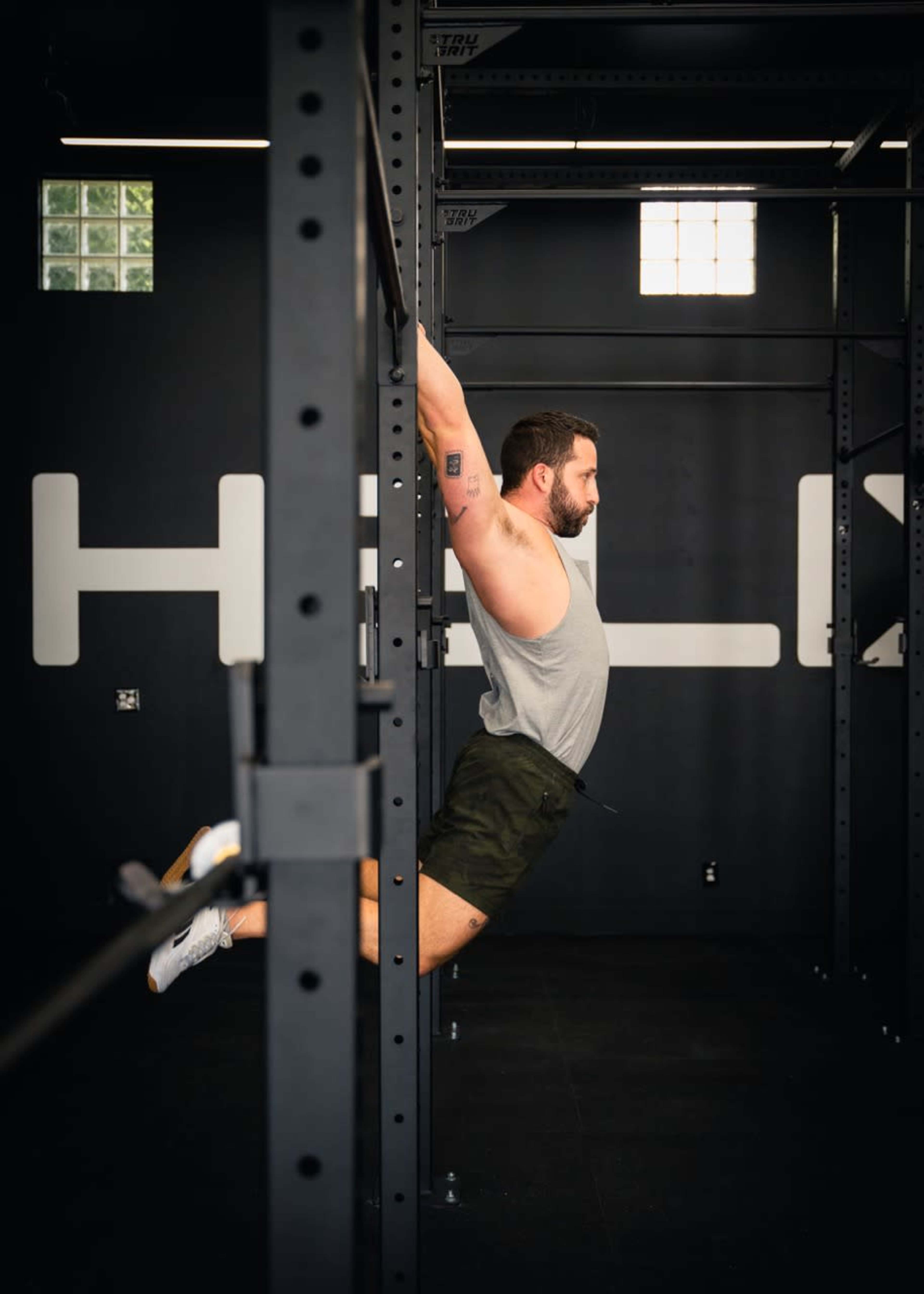 A man performs a pull-up on a metal gym structure in a fitness facility.