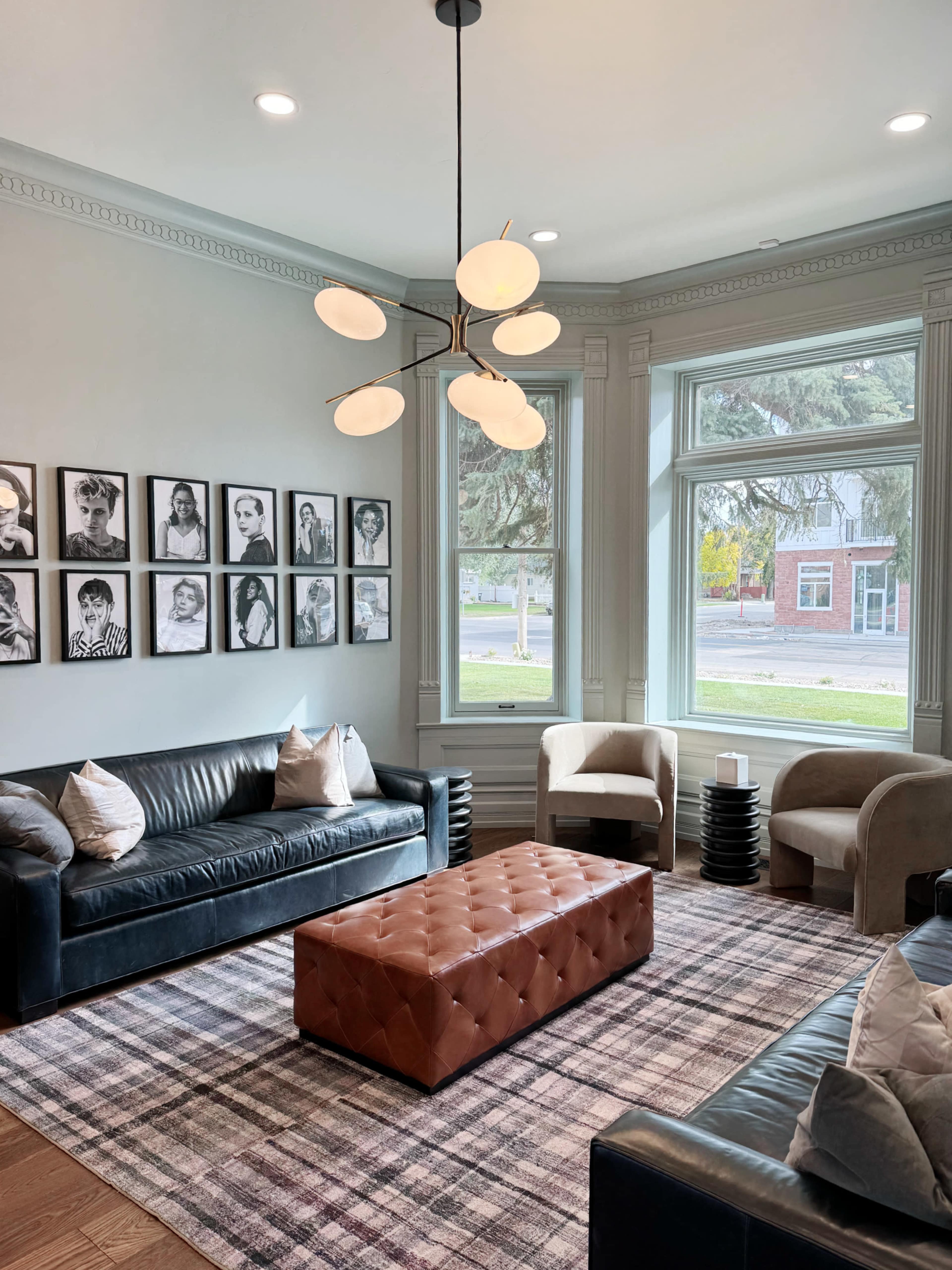 A cozy living room with two sofas, a tufted ottoman, and a gallery wall of framed black-and-white portraits.