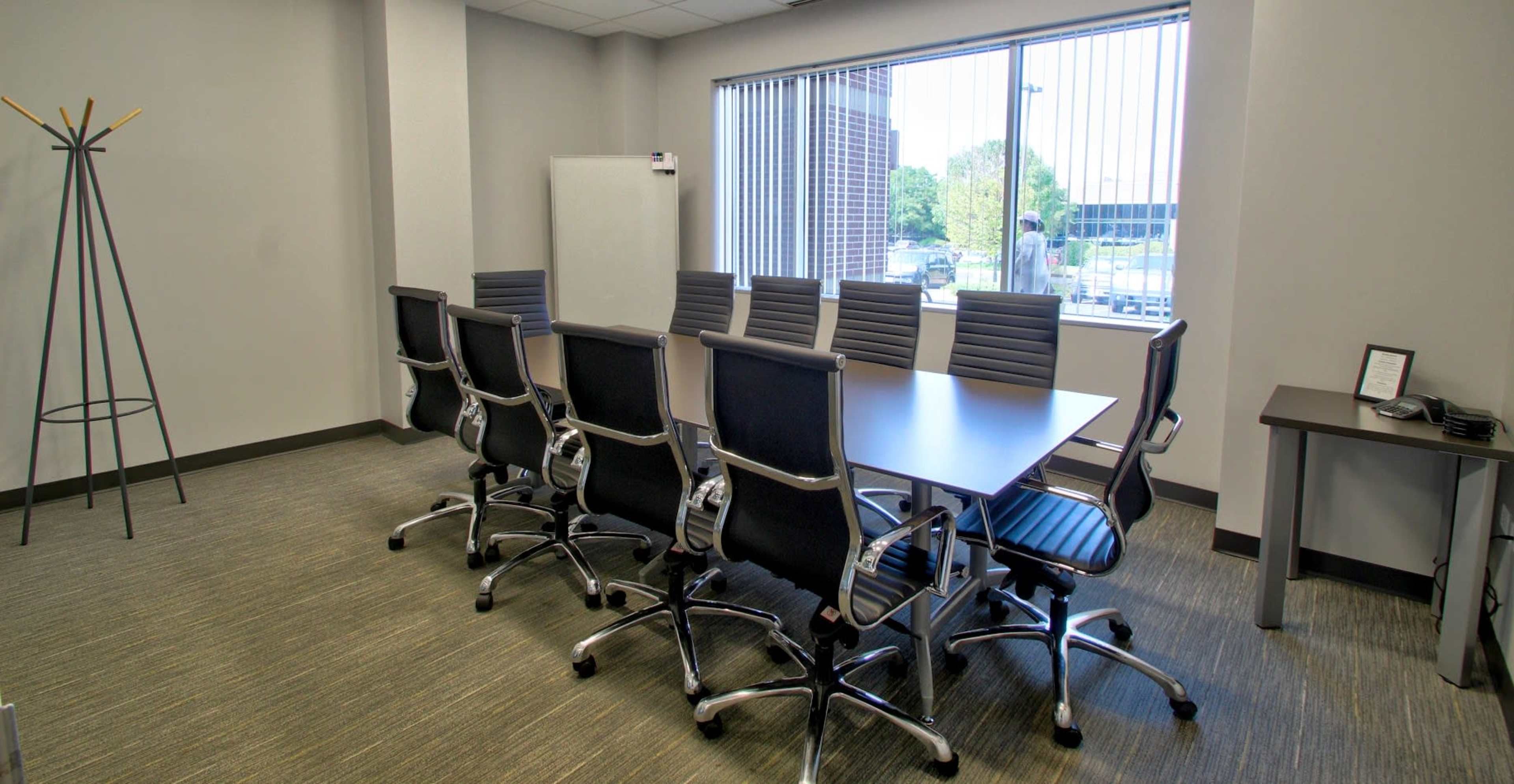 A conference room features a long table surrounded by eight ergonomic chairs and a window overlooking an outdoor view.