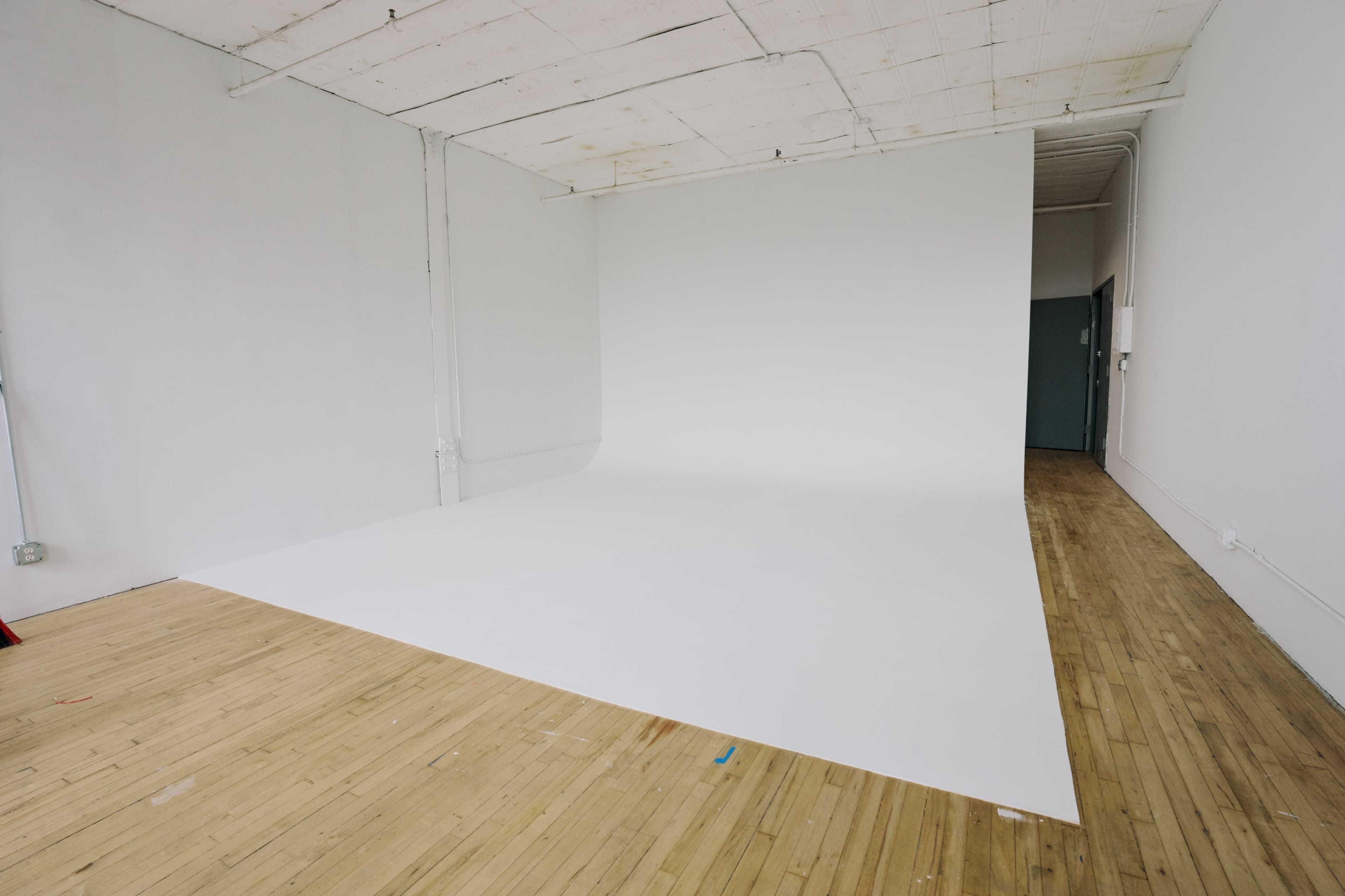 The image shows a spacious photography studio with a seamless white backdrop and wooden flooring.