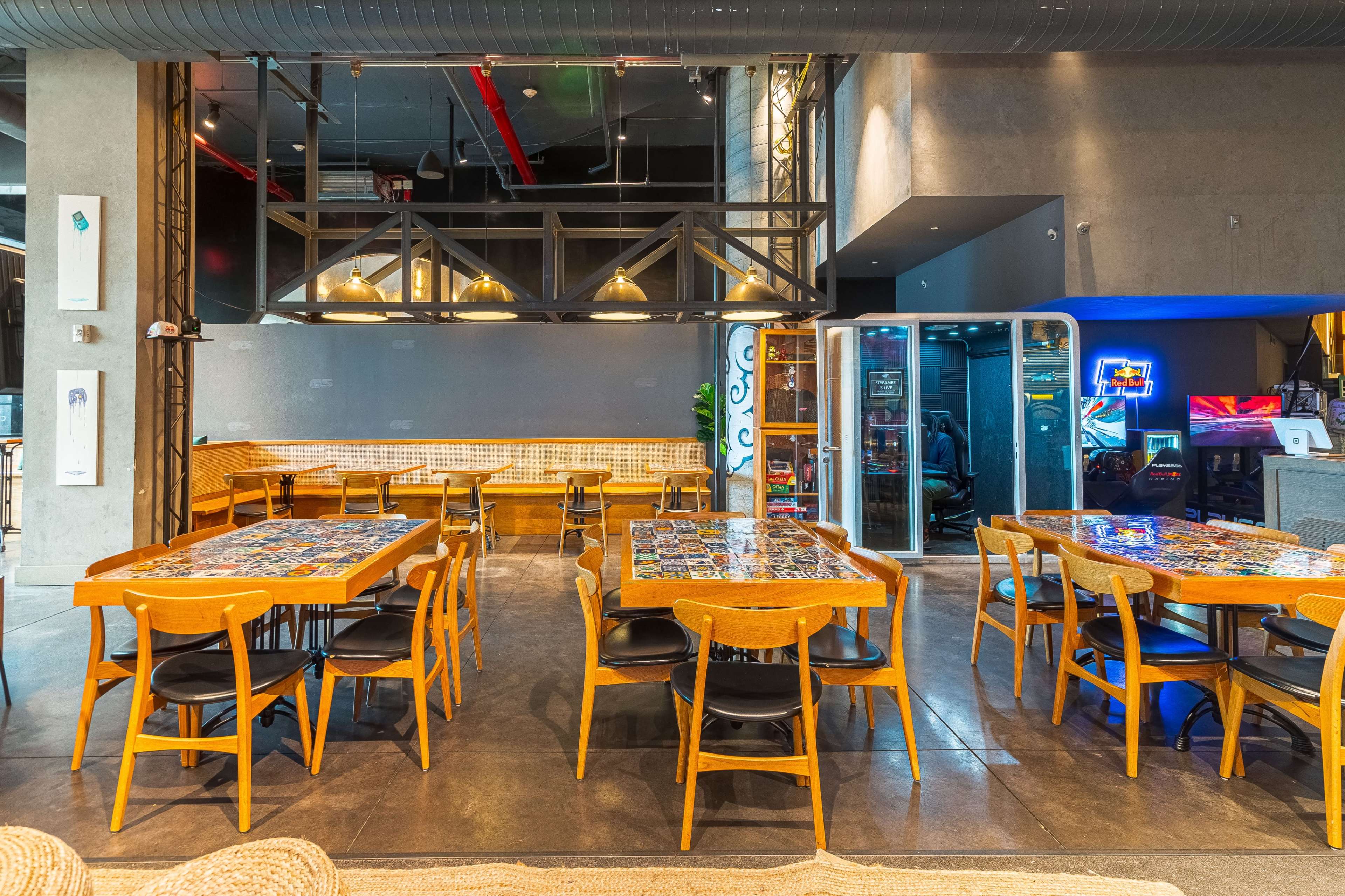 A modern restaurant interior with wooden tables and black chairs arranged in a spacious setting, featuring a mix of vibrant decor and industrial elements.