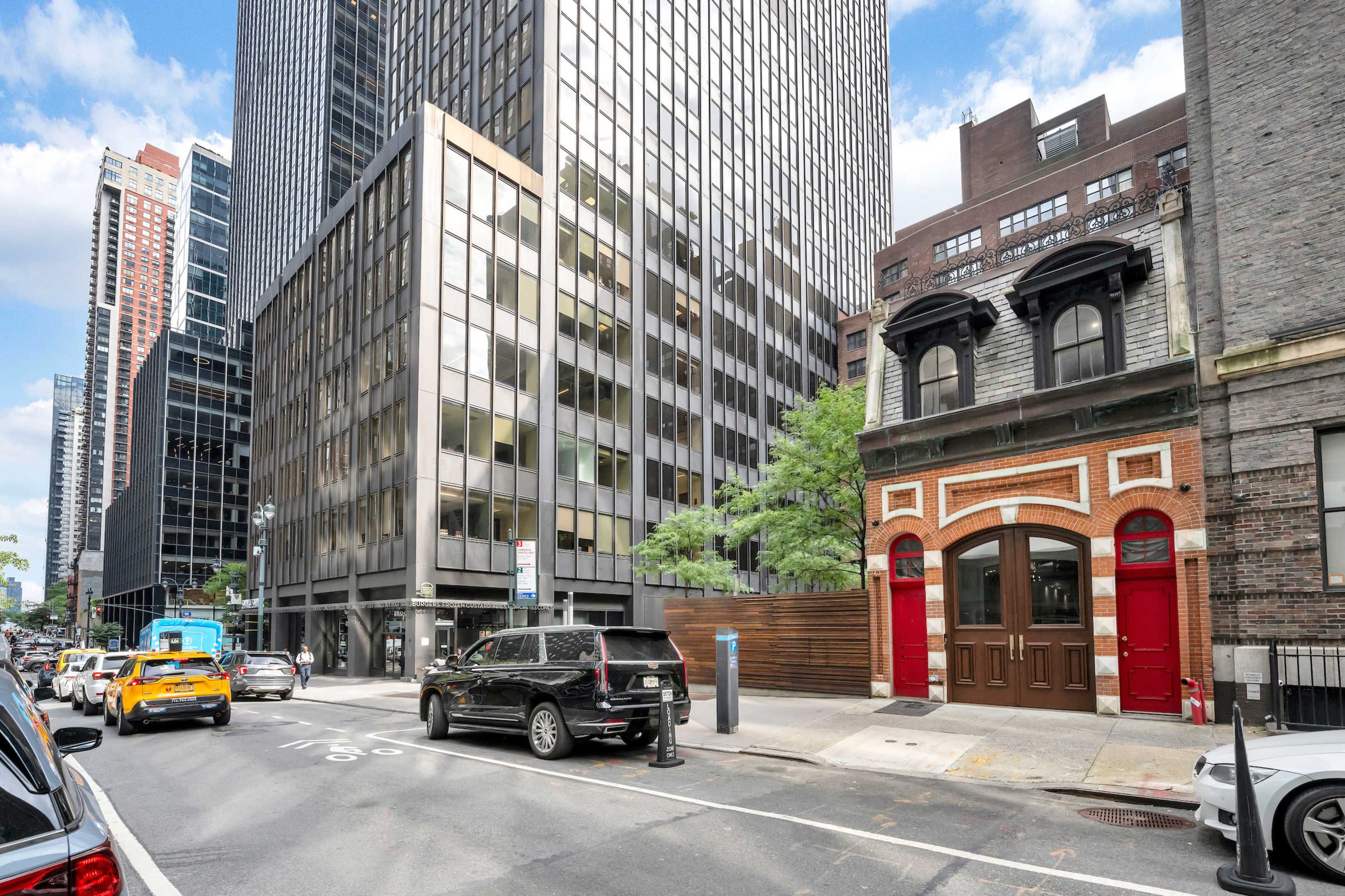 A city intersection features a mix of modern high-rise buildings and a historic brick structure with red doors.