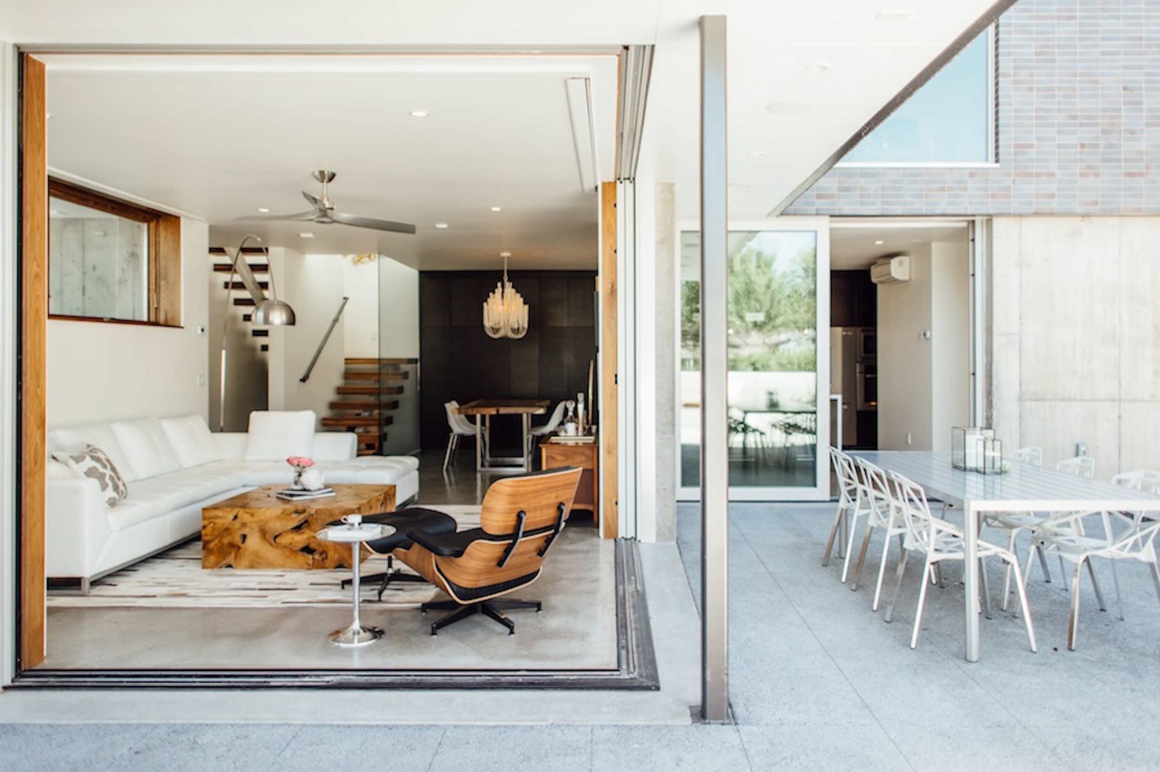 The image shows a modern, open-concept living space that connects an indoor lounge area with an outdoor dining area.