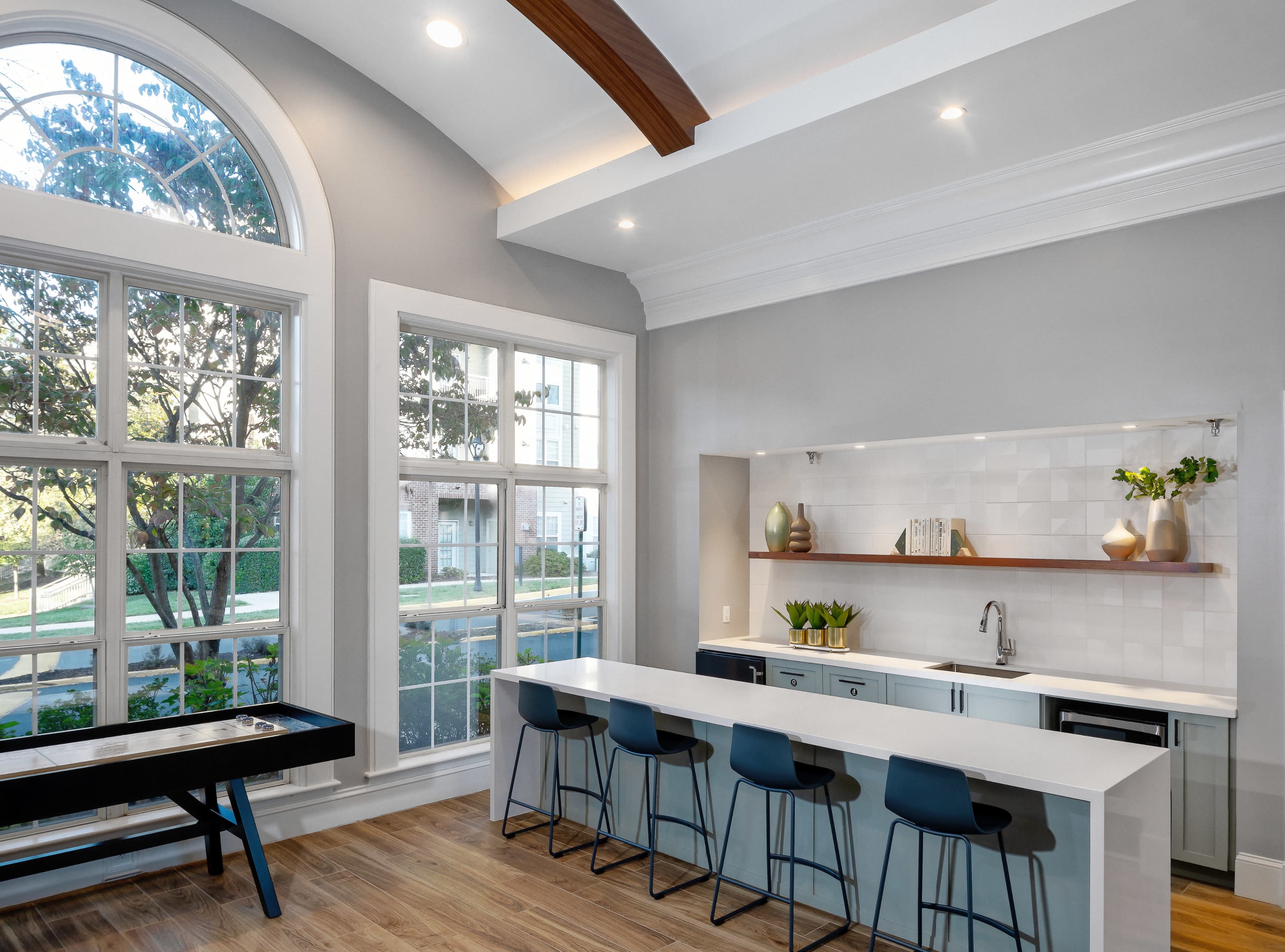 A modern kitchen features a large white island with barstools, large windows allowing natural light, and minimalist shelving with decorative items.