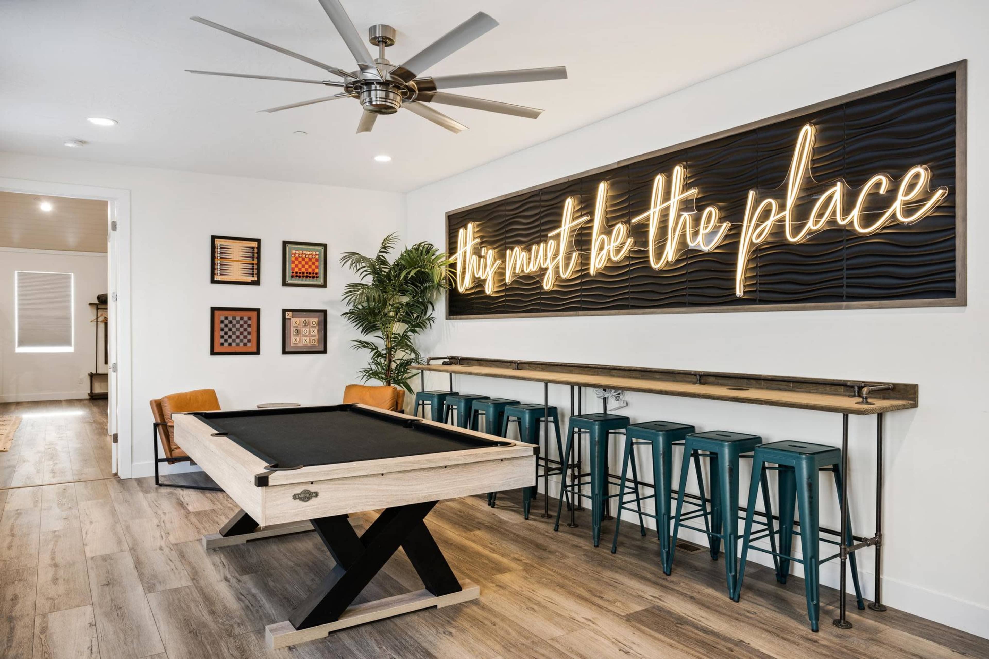 A game room with a pool table, bar stools, and a neon sign that reads "This must be the place."
