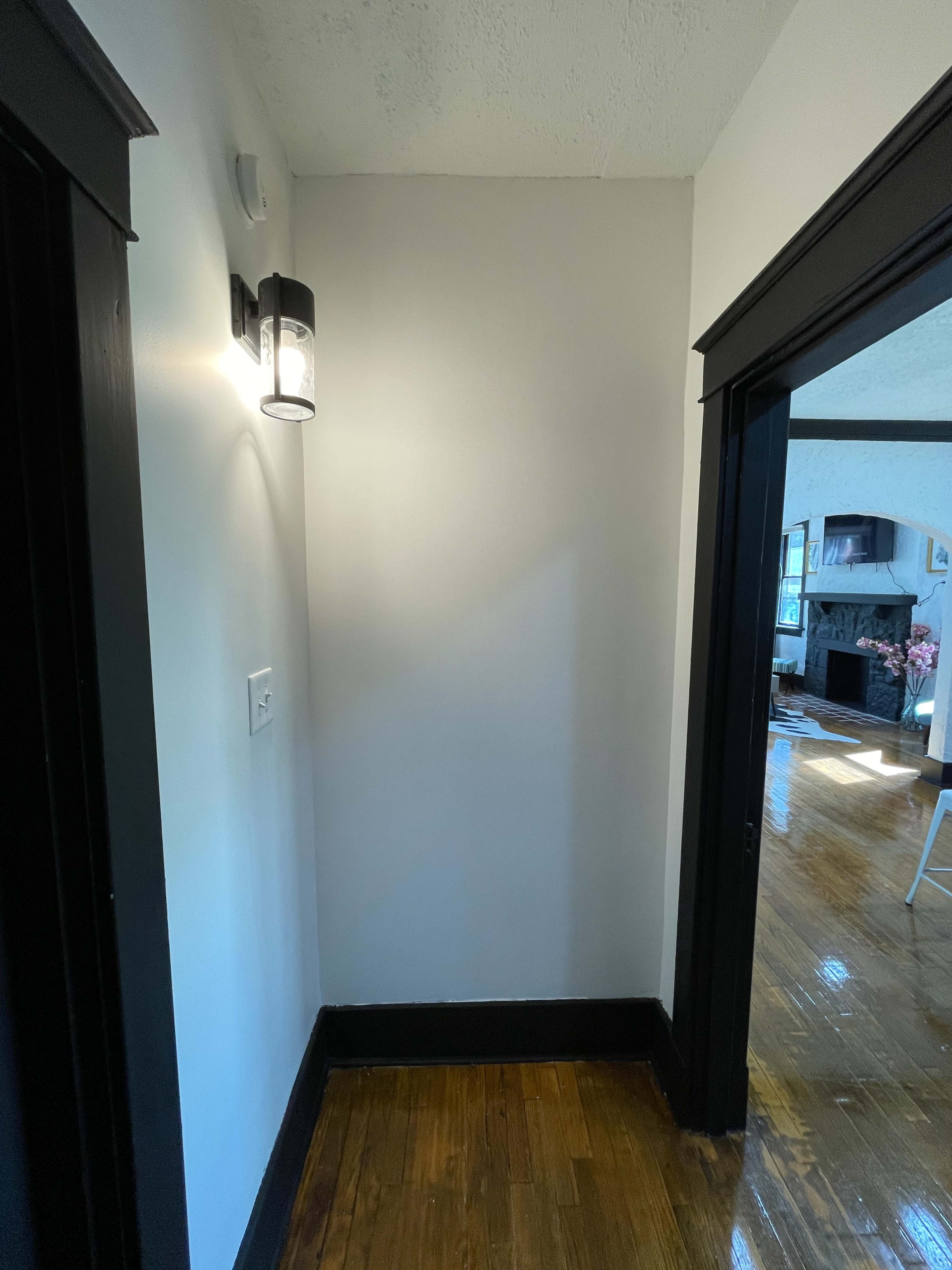 A corner of a hallway with a light fixture on the wall and a doorway leading to another room.