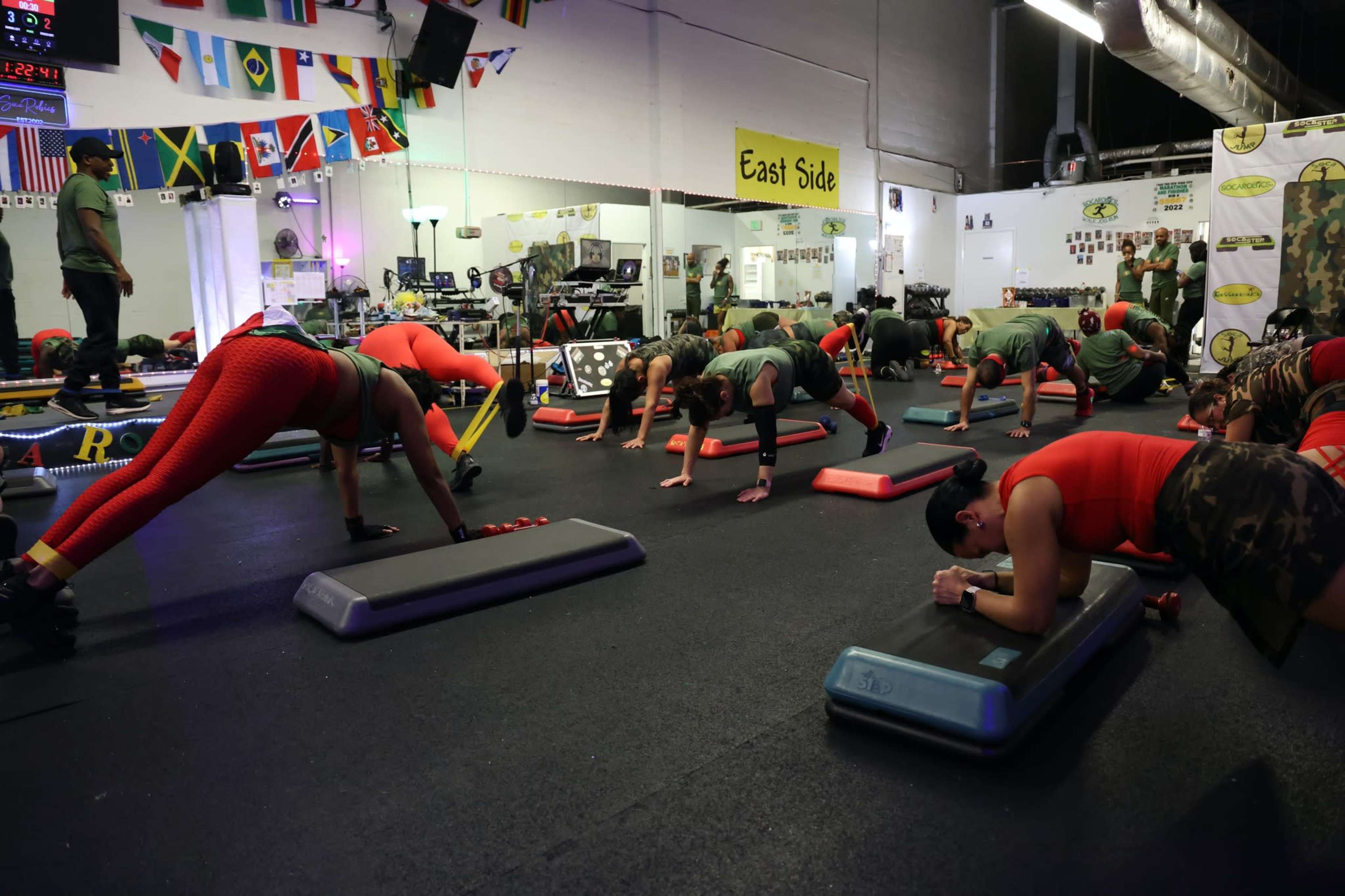 A fitness class takes place in a gym where participants perform various exercises, featuring individuals in workout attire engaged in activities on exercise mats.