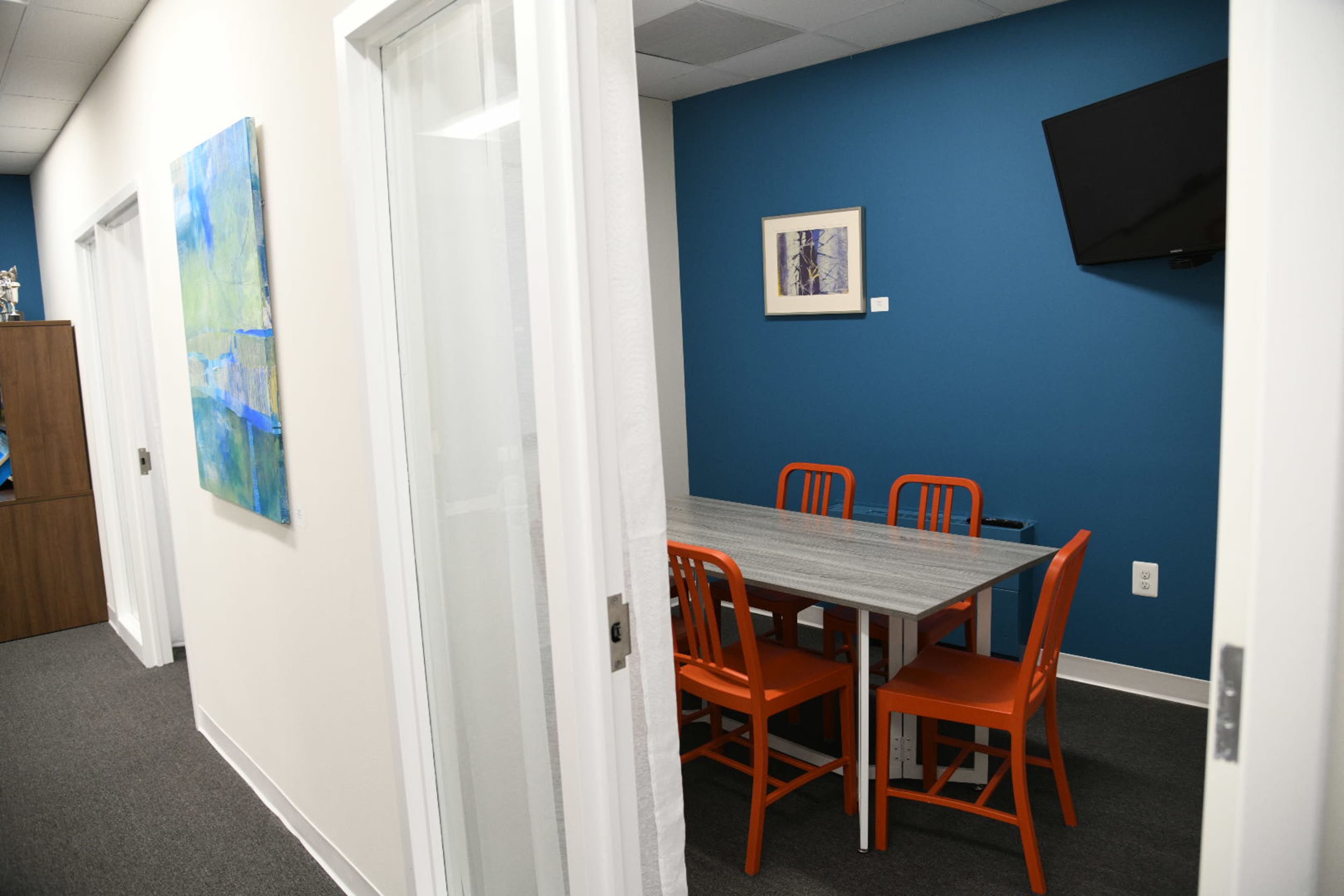A brightly colored meeting room with an orange and gray table surrounded by orange chairs, situated between two white walls with a blue accent wall.