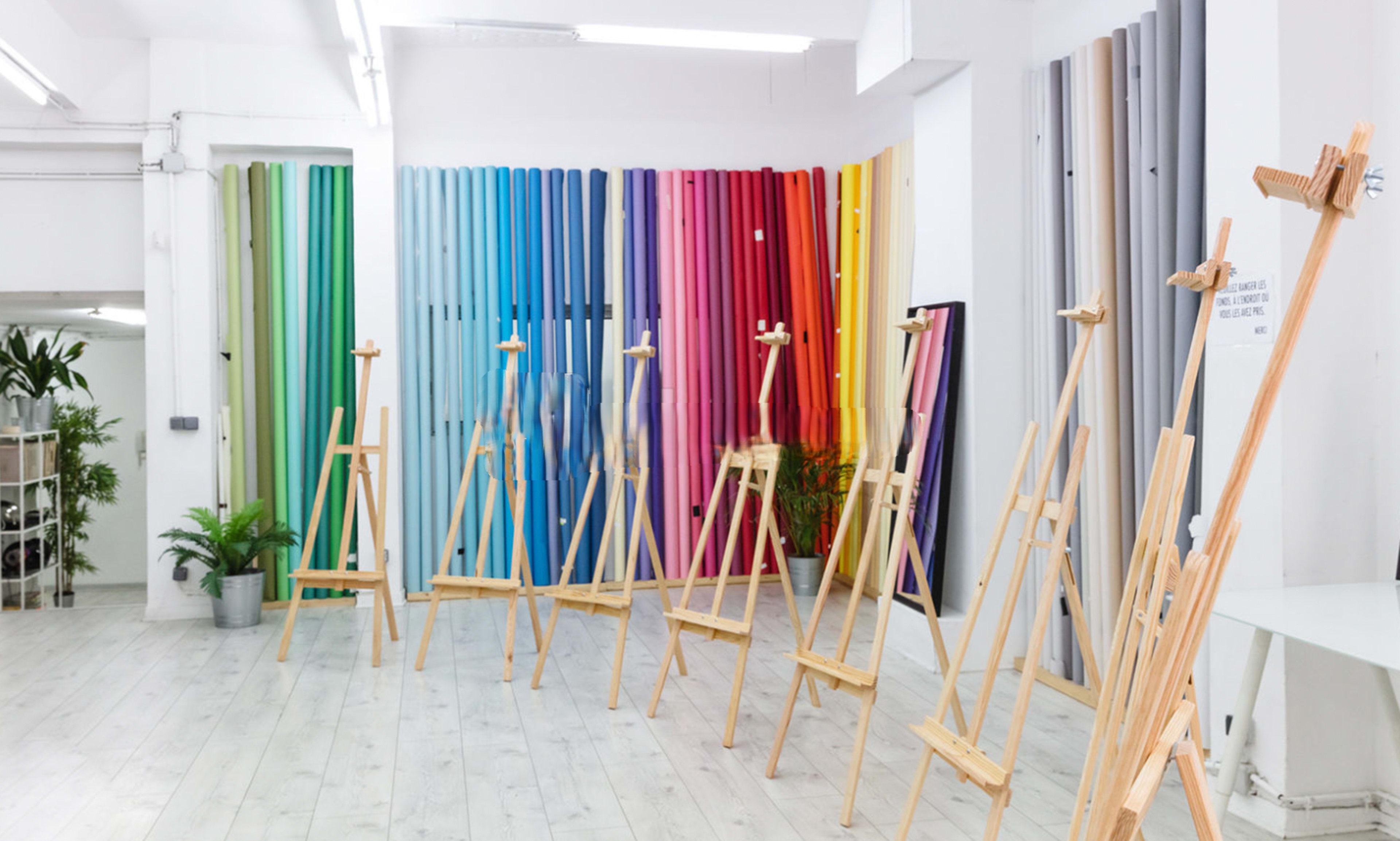 A bright art studio featuring wooden easels arranged in rows against a backdrop of colorful vertical panels.