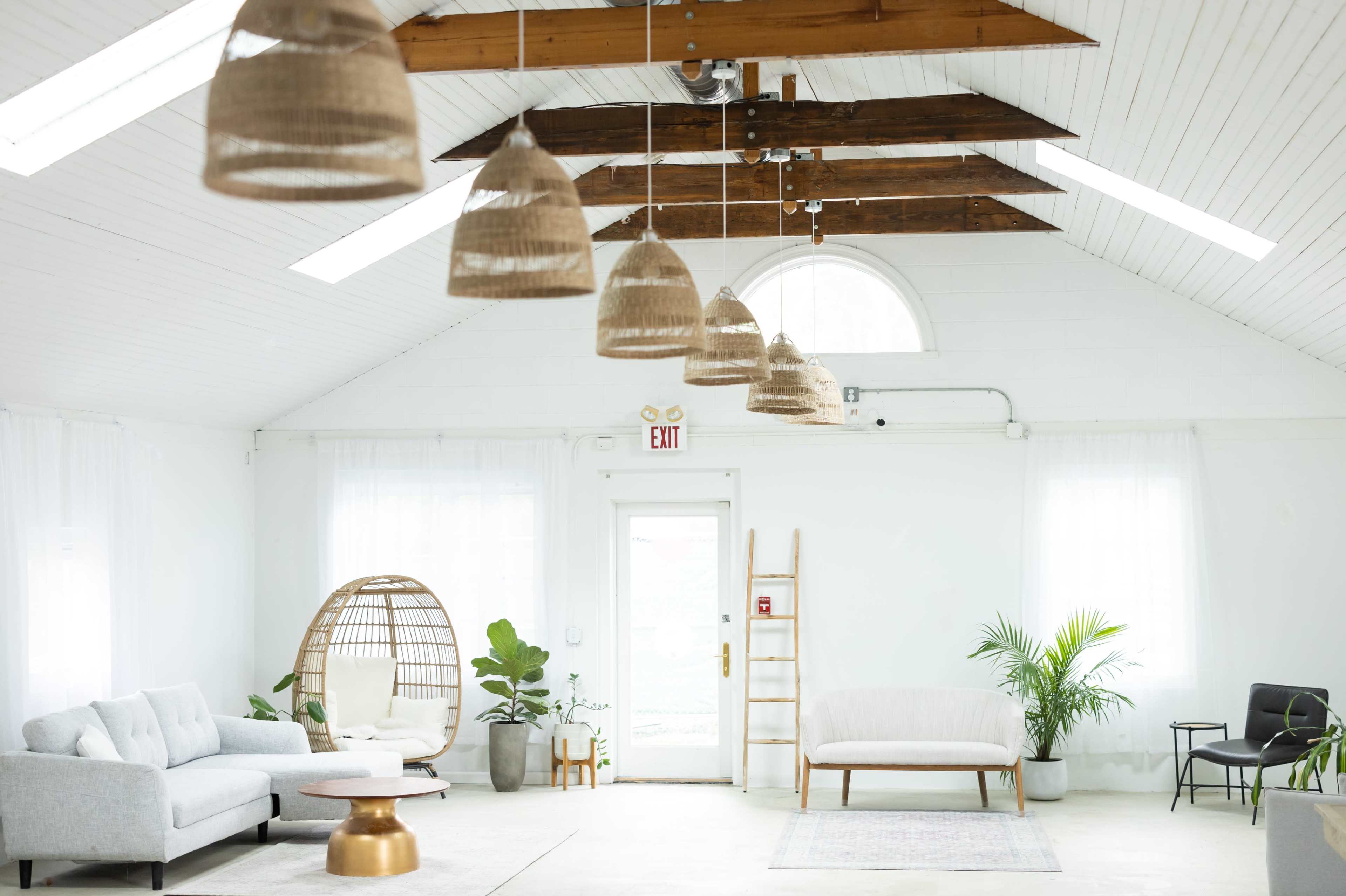 A well-lit, open interior space features modern furniture, tall ceilings with wooden beams, and decorative hanging light fixtures.