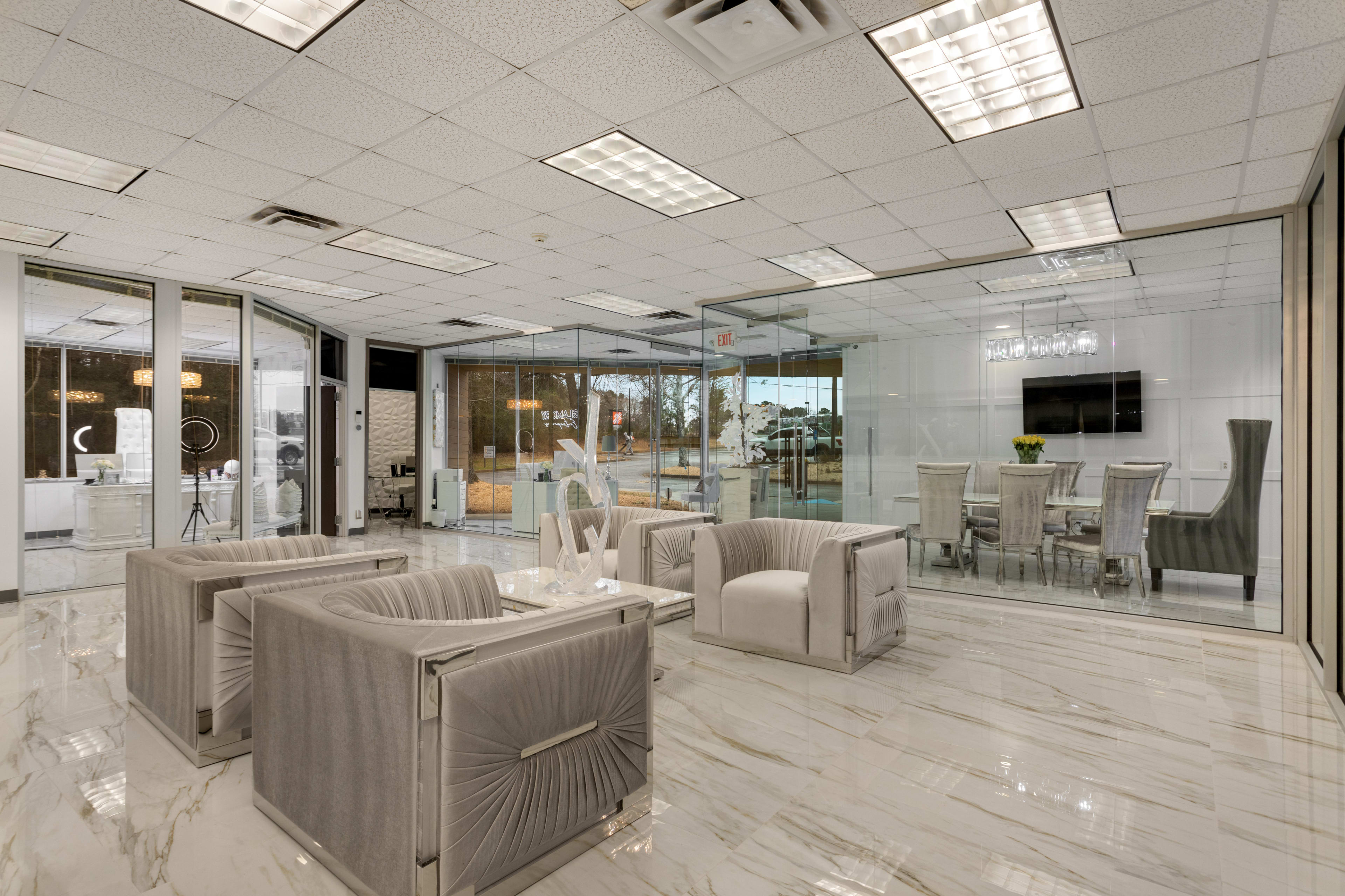 A modern office space with glass walls, marble flooring, and a seating area featuring plush armchairs.
