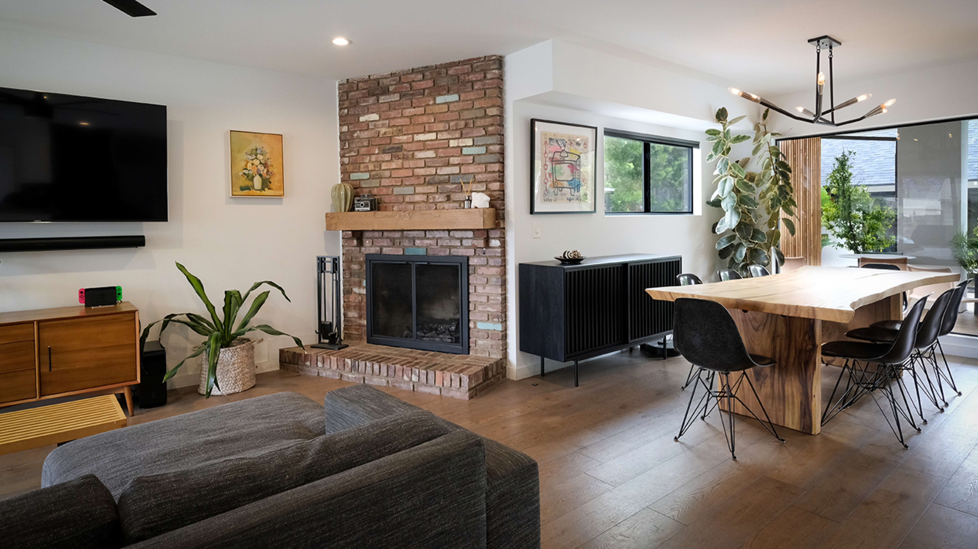 A modern living space with a brick fireplace, a wooden dining table, and large windows overlooking an outdoor area.