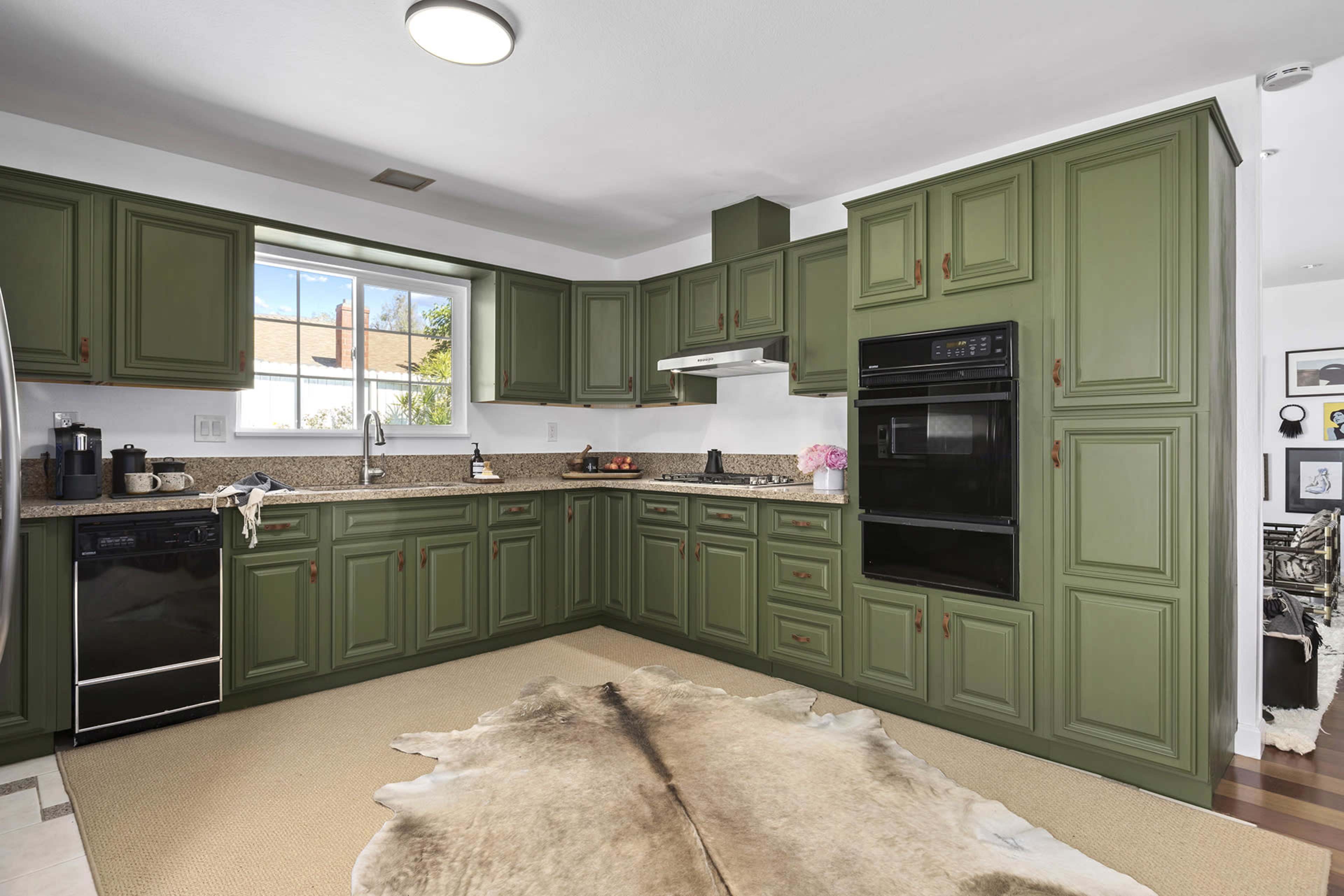 The image shows a kitchen with green cabinetry, a granite countertop, and a window overlooking an outdoor view.