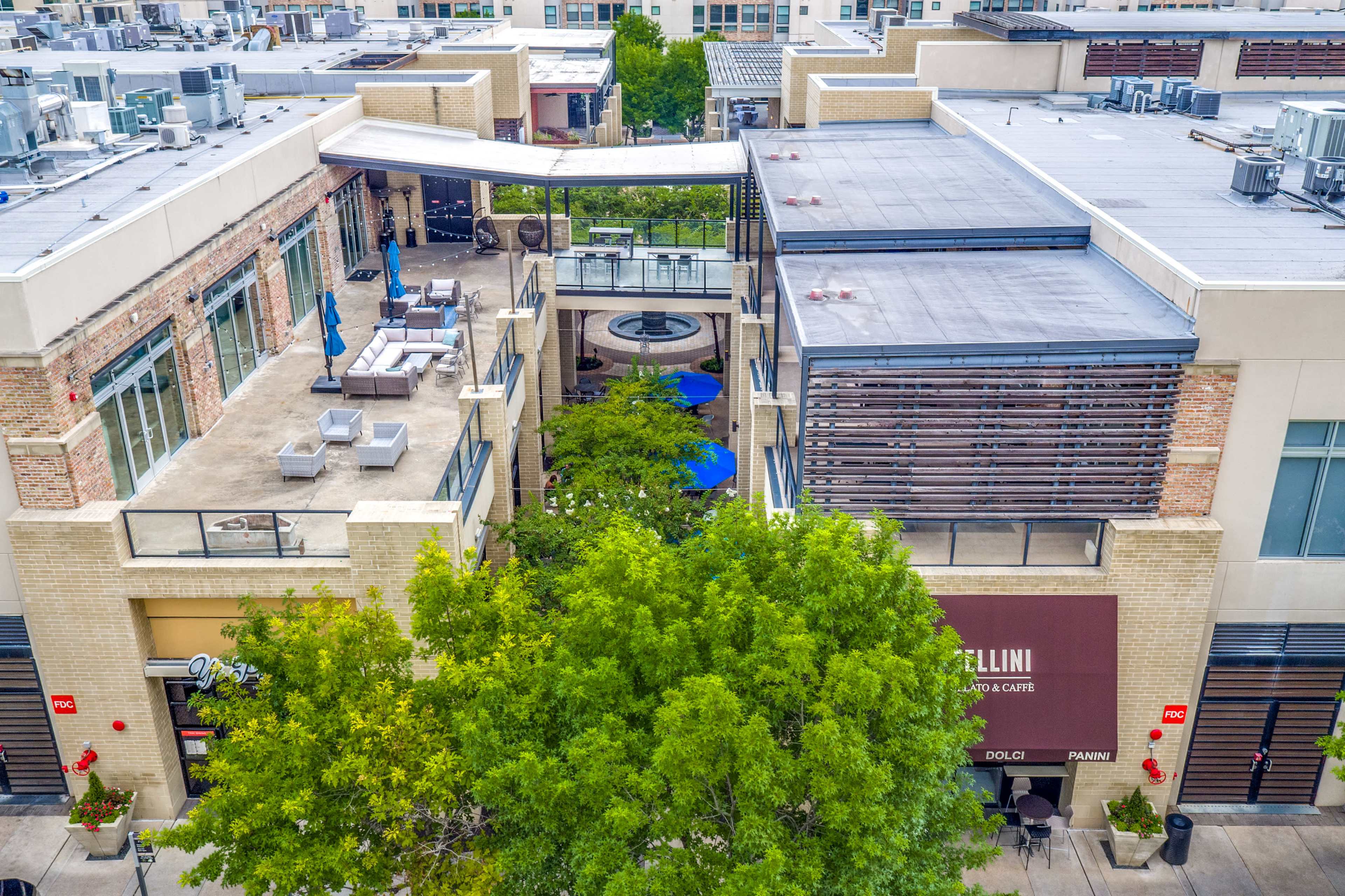 A multi-level commercial building featuring a terrace area with seating, surrounded by greenery and other storefronts.