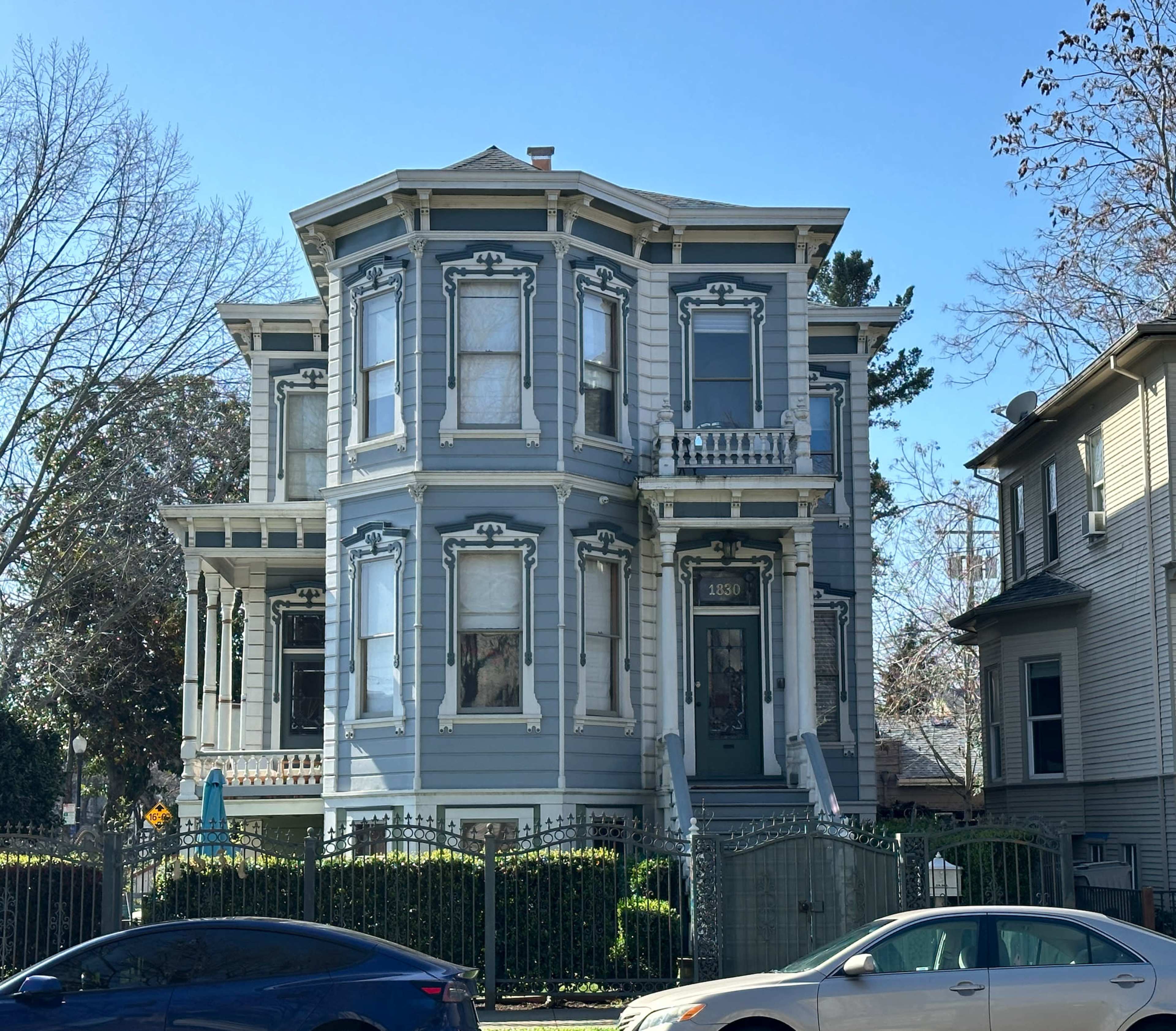 A large Victorian-style house painted blue, featuring intricate architectural details and a fenced yard.