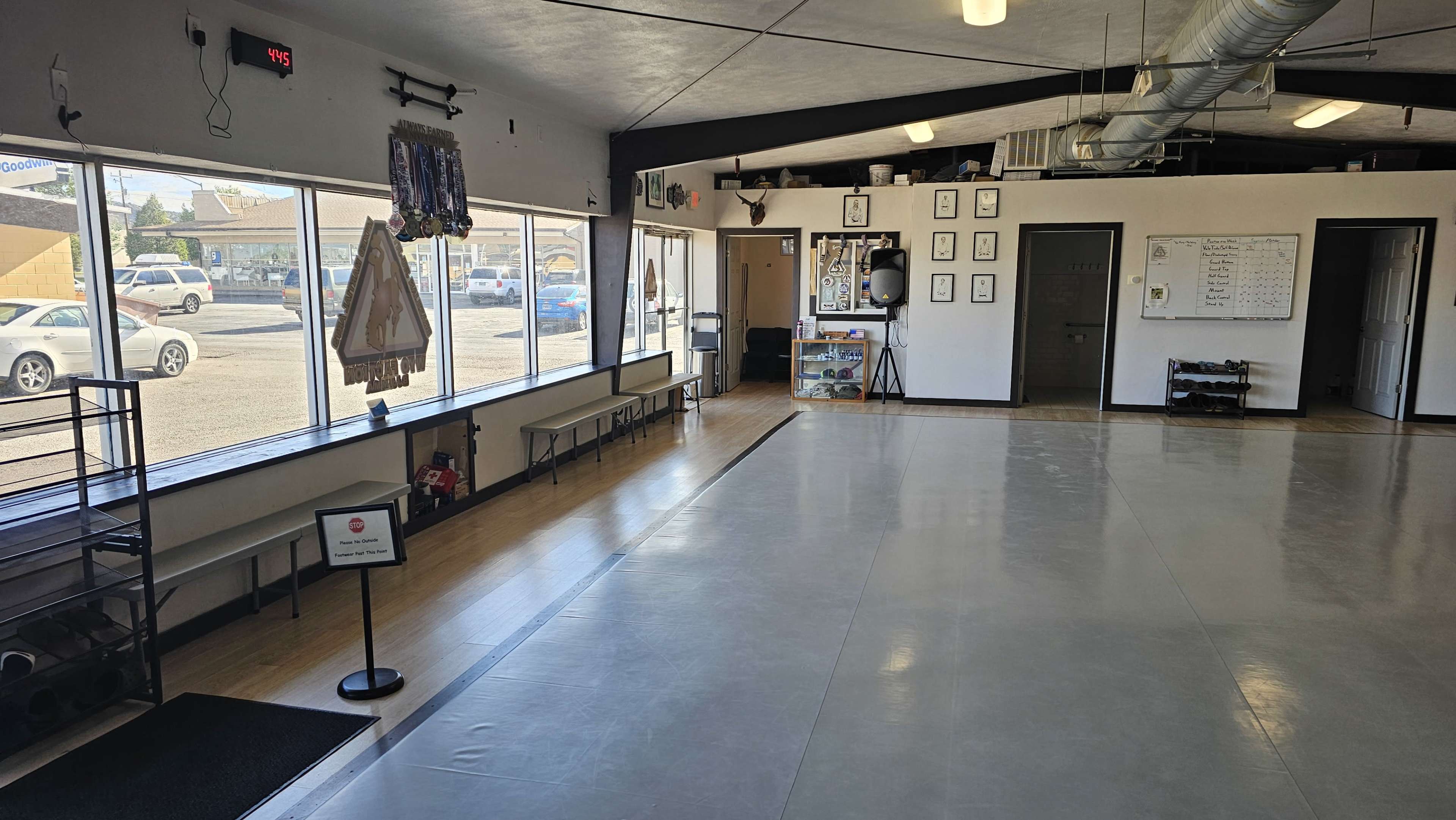 The image shows an empty indoor space with a smooth floor and large windows letting in natural light, along with a small reception area and benches.