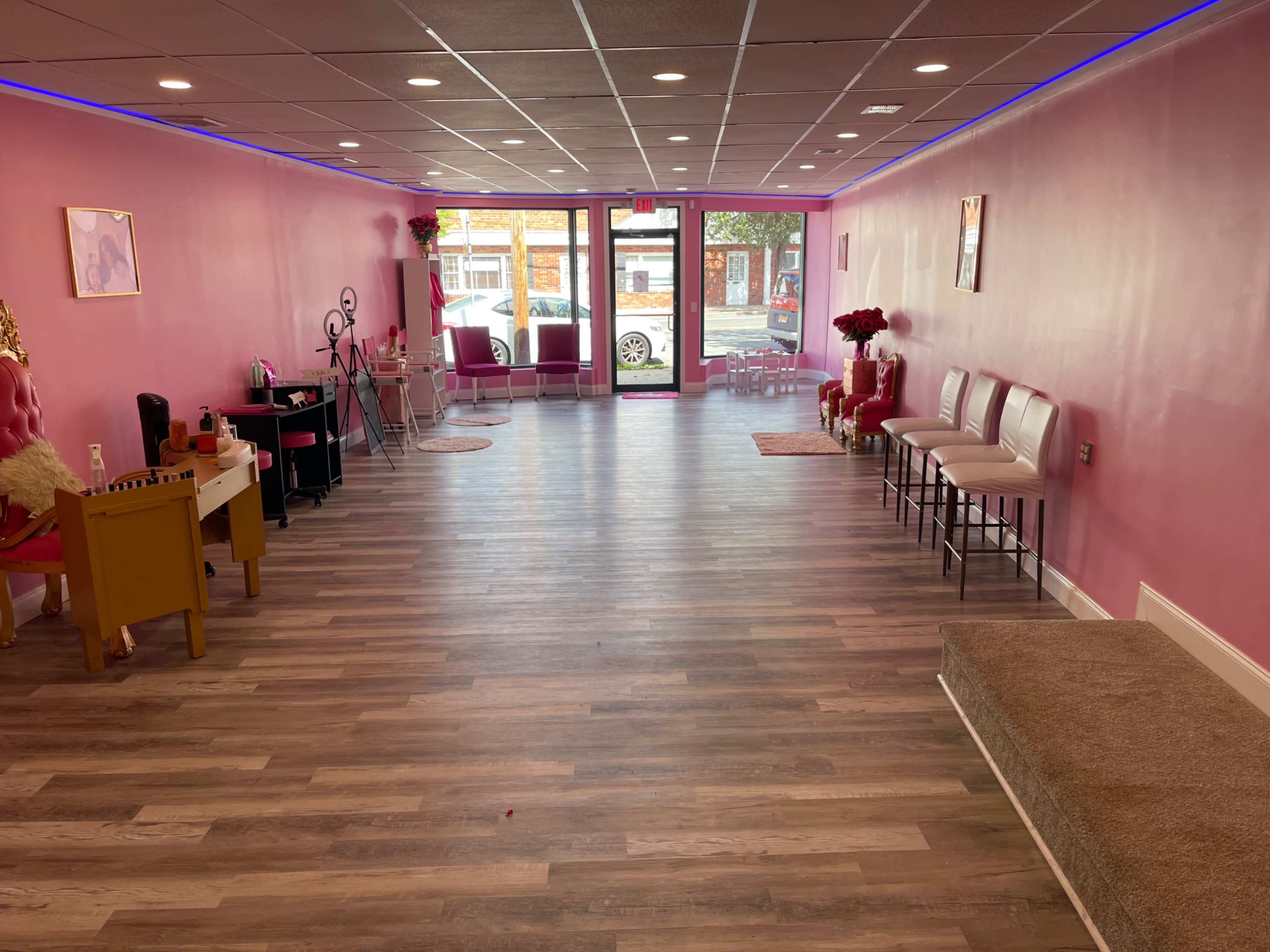 A spacious pink-themed salon interior with wooden flooring, featuring a waiting area with chairs and a reception desk.