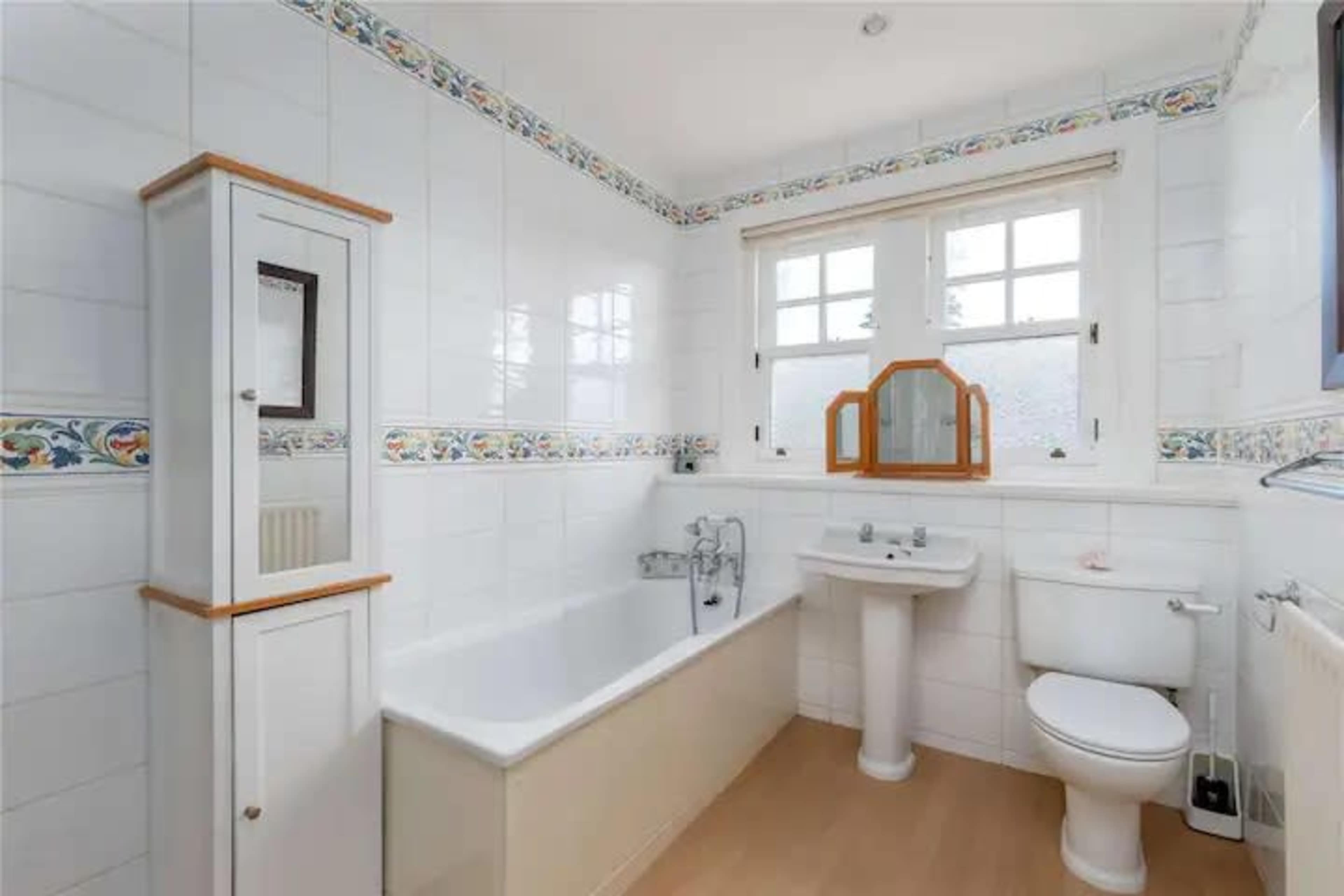 A bathroom with a bathtub, sink, toilet, and decorative tiled border along the walls.