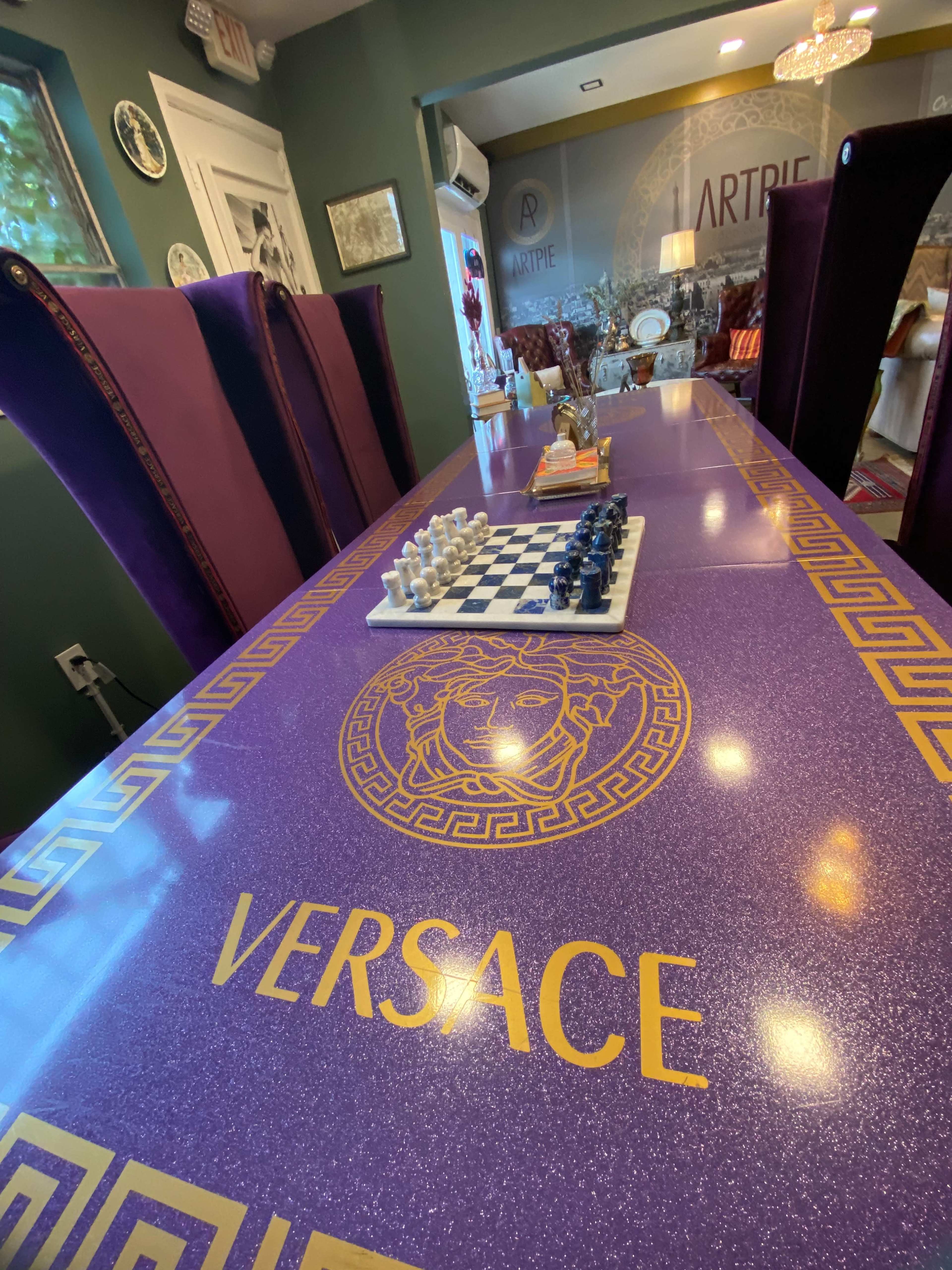 A long purple dining table with a Versace logo and a chessboard set up with white and black pieces in the center.